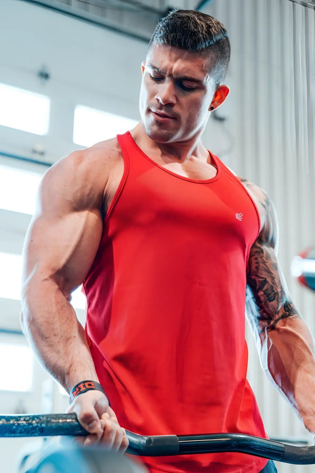 A man wearing a vibrant red fast-dry bodybuilding workout stringer tank top with a small logo on the chest