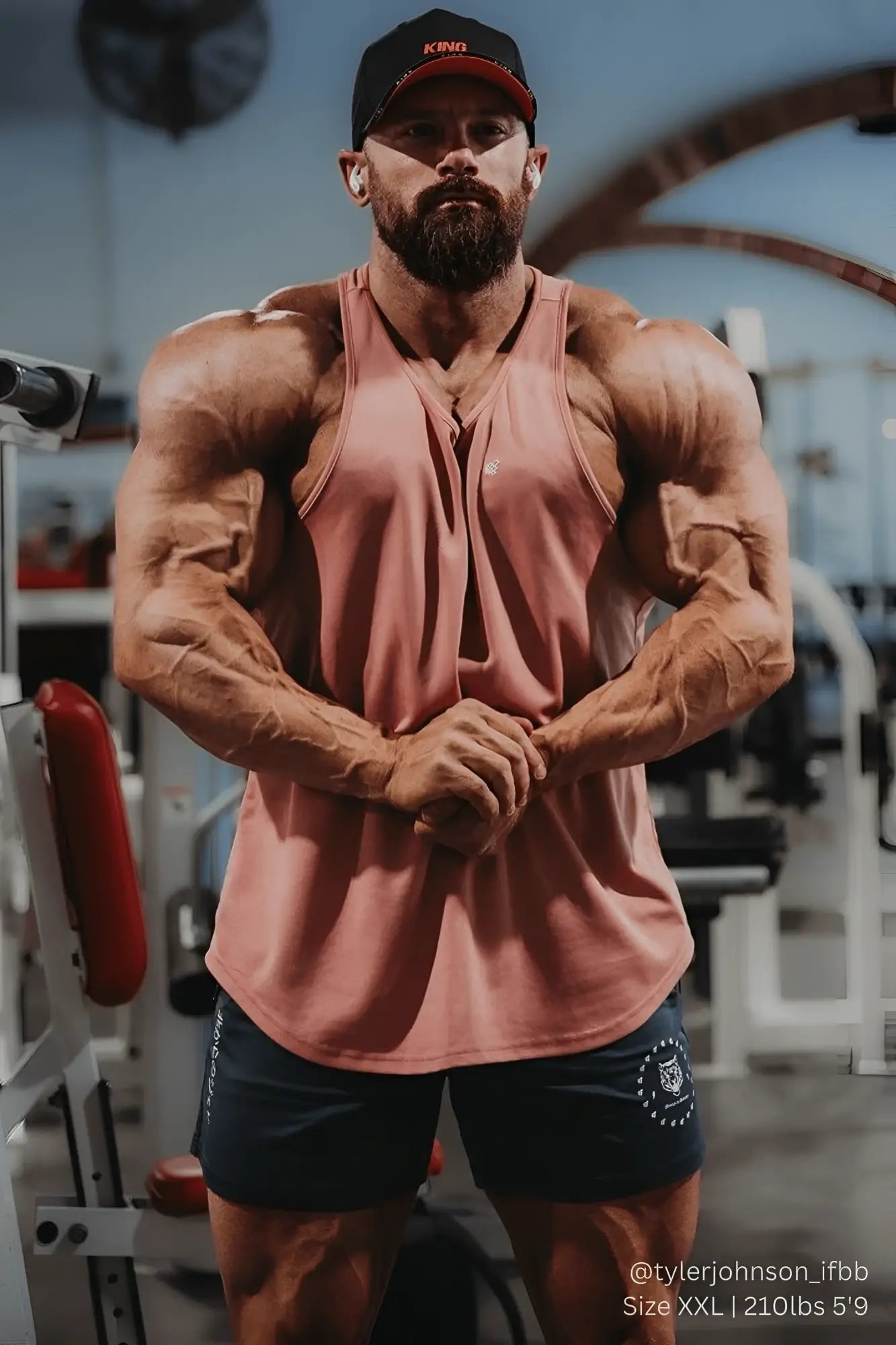 A muscular man wearing a dusty rose sleeveless salmon stringer tank top with v-neck and side slits for bodybuilding workouts