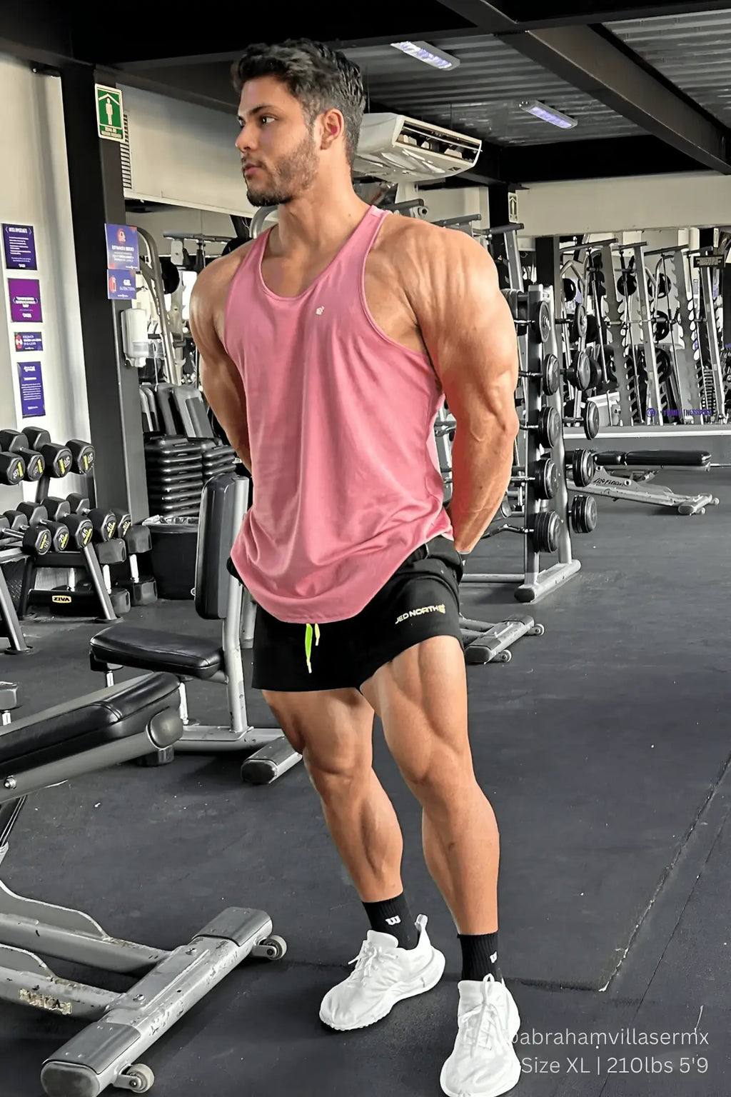 A muscular man wearing a salmon jed north fast-dry bodybuilding workout stringer with black shorts and neon green drawstrings