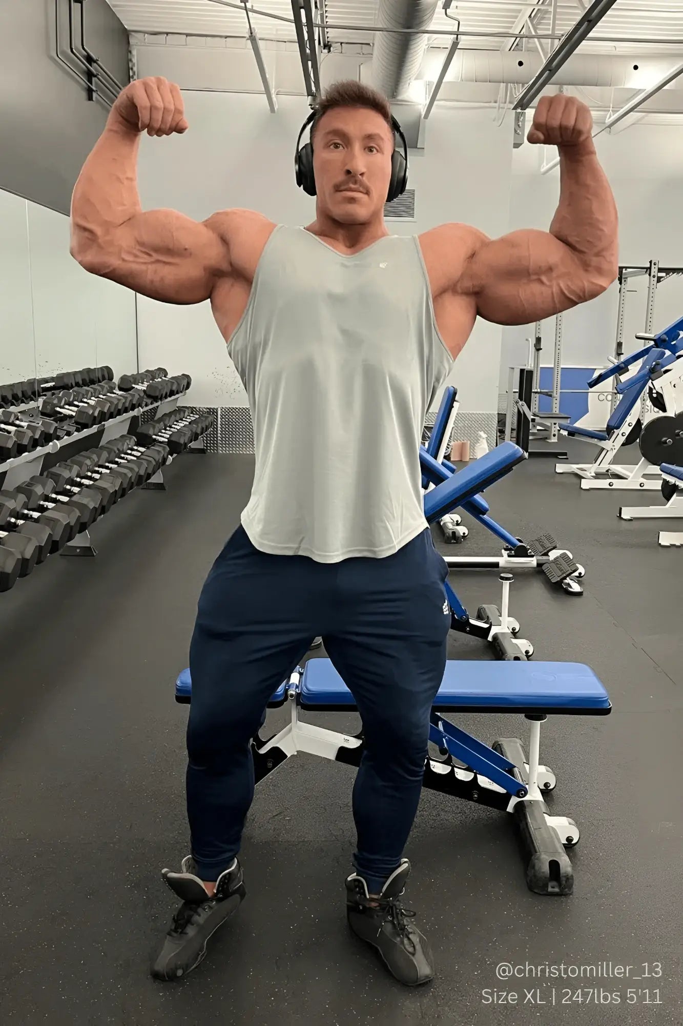 Muscular man wearing Jed North fast-dry bodybuilding workout stringer in silver with dark blue athletic pants