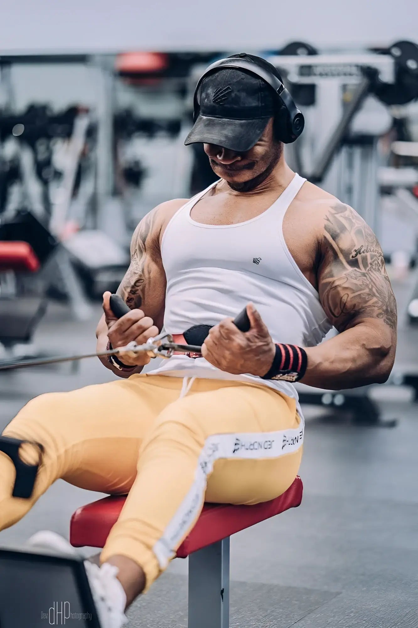 A muscular man wears a jed north fast-dry bodybuilding workout stringer in white while using a cable machine