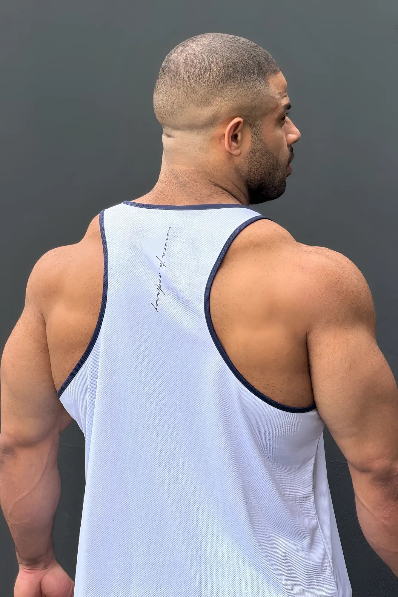 Back view of fast-dry bodybuilding workout stringer tank top in white with navy trim and subtle cursive logo