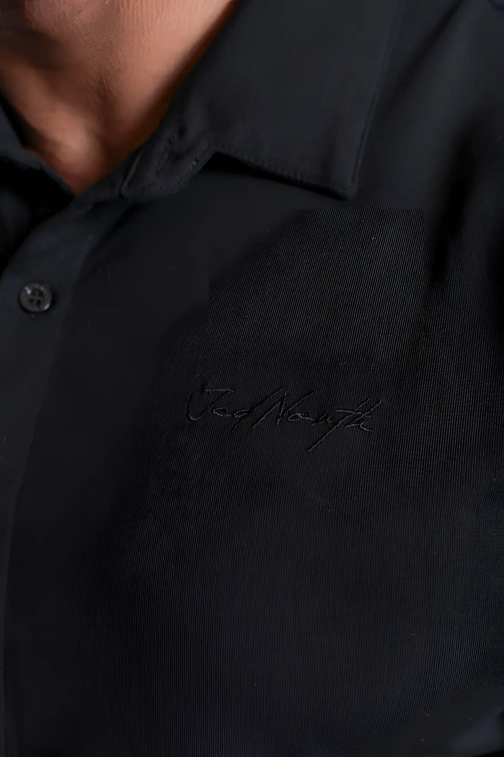 Black textured flex premium stretch polo shirt in onyx black with subtle embroidered signature on the chest