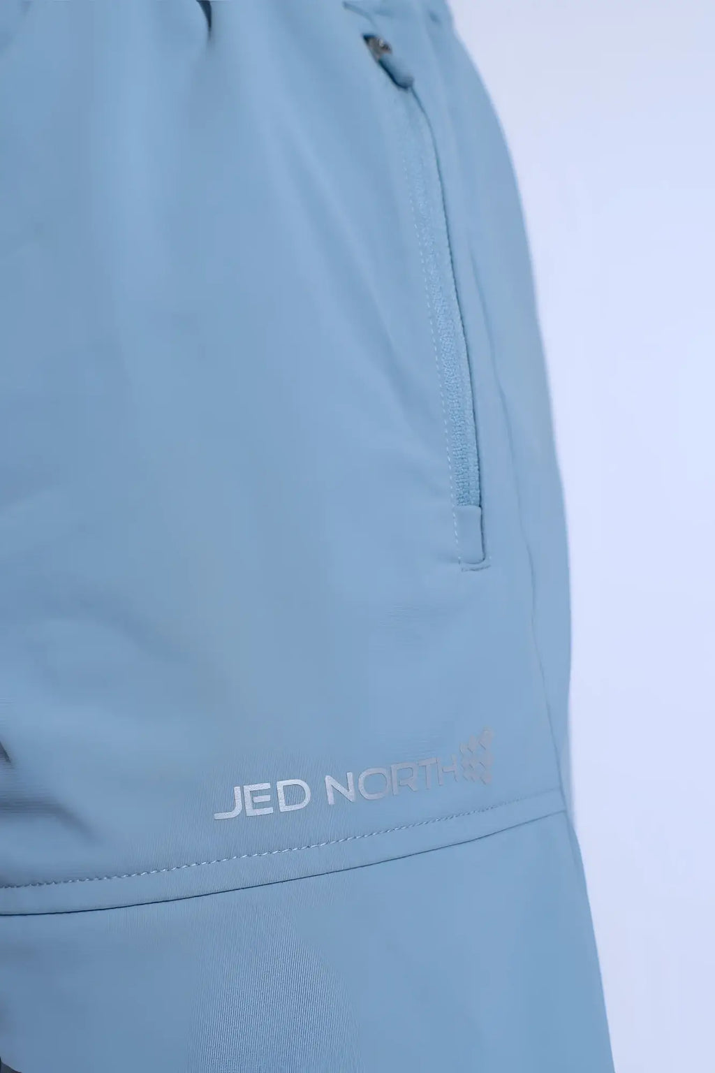 Fortis men’s light blue athletic shorts with subtle textured fabric and zippered side pocket featuring jed norris logo