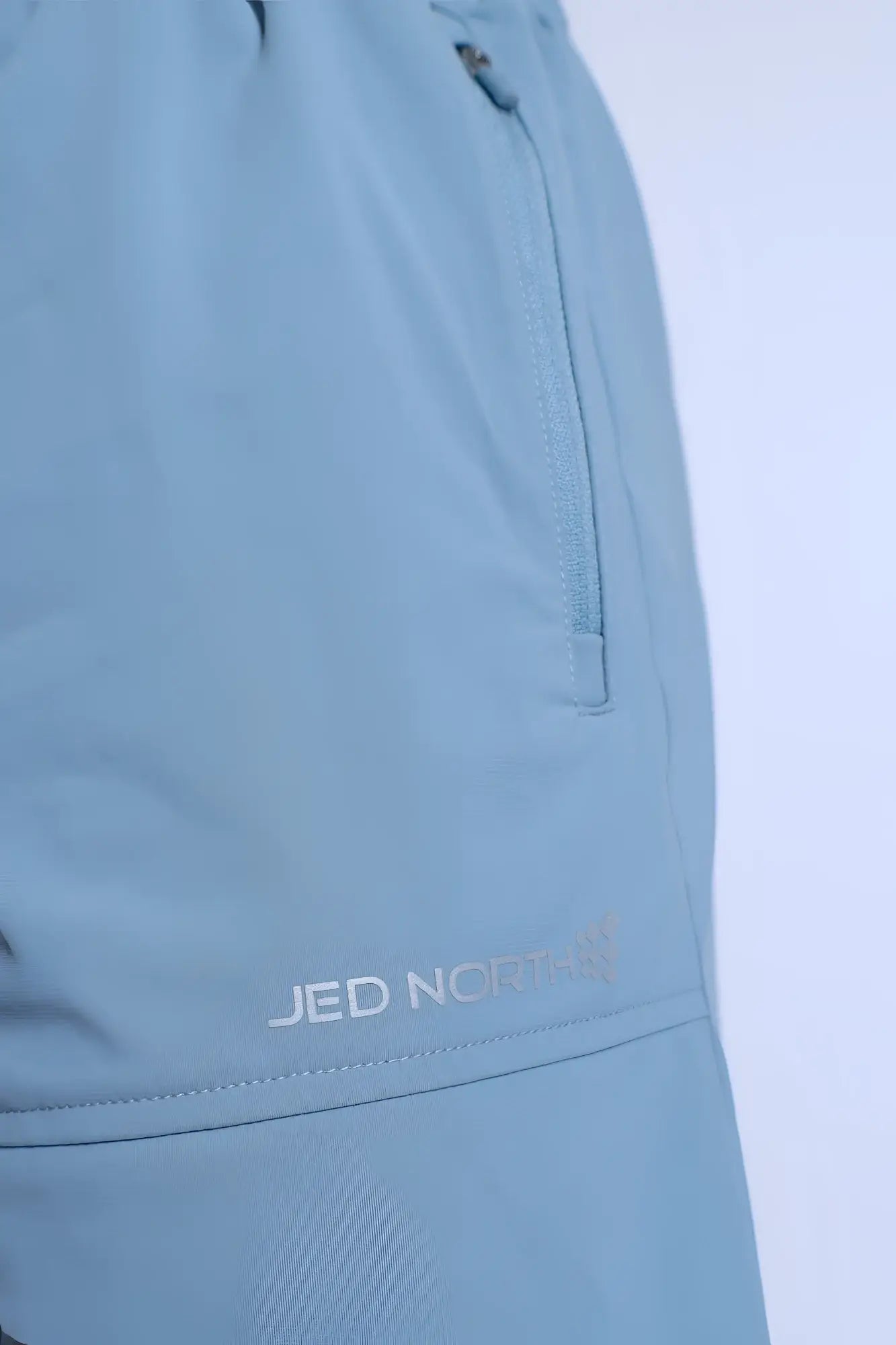 Fortis men’s light blue athletic shorts with subtle textured fabric and zippered side pocket featuring jed norris logo