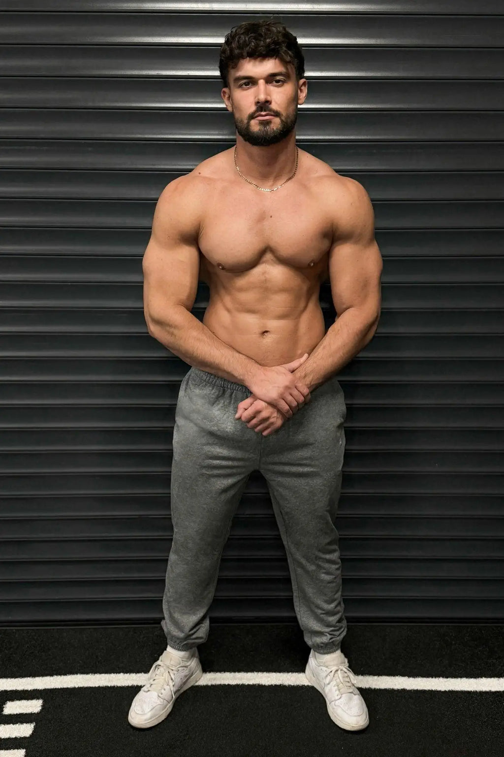 A muscular man wearing gray Jed North French Terry athletic training joggers and white sneakers stands confidently