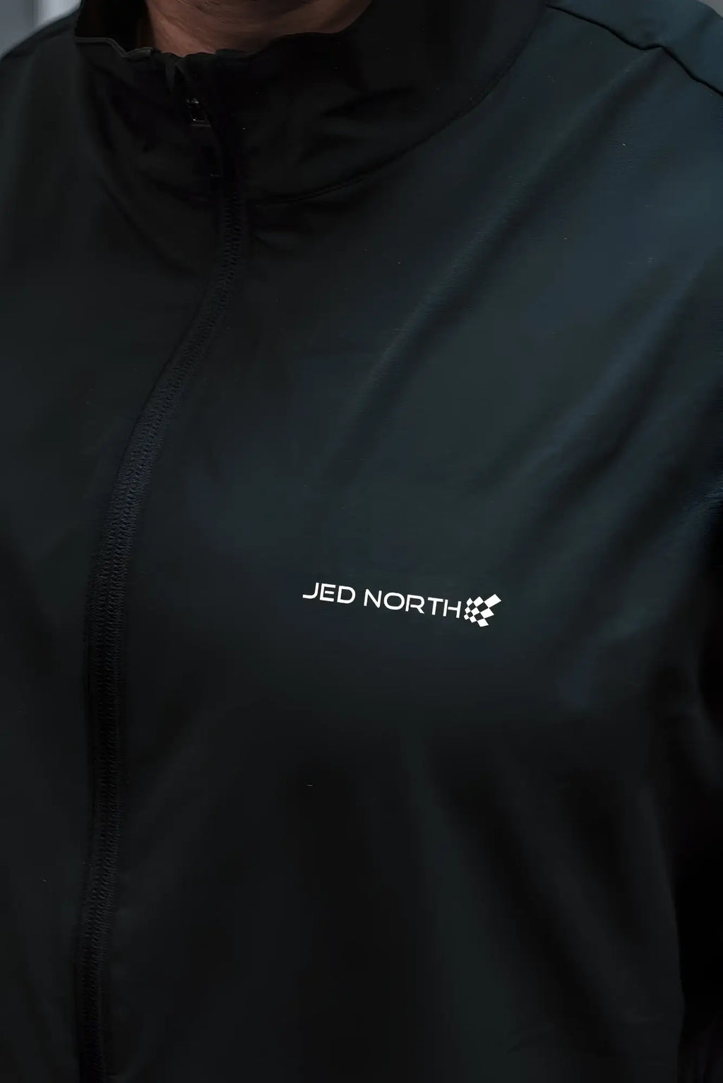 Black full-zip training jacket with white jed north logo and checkered flag emblem on the chest