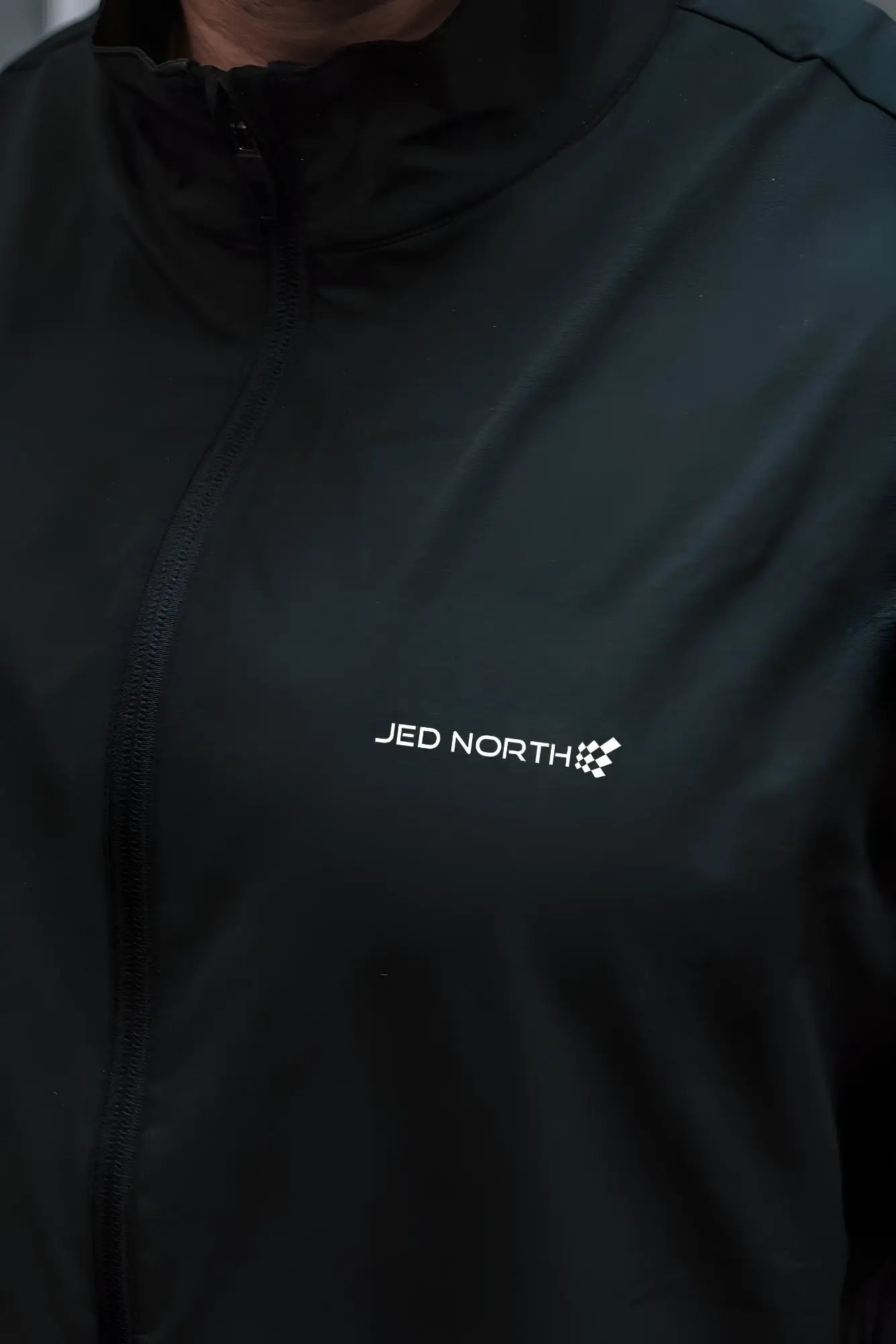 Black full-zip training jacket with white jed north logo and checkered flag emblem on the chest