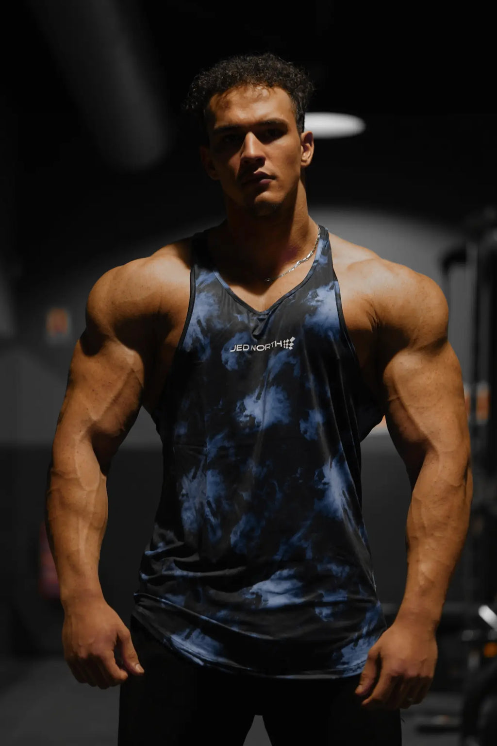 A dark blue and black tie-dye v-neck muscle stringer tank top with jed north logo in white across the chest
