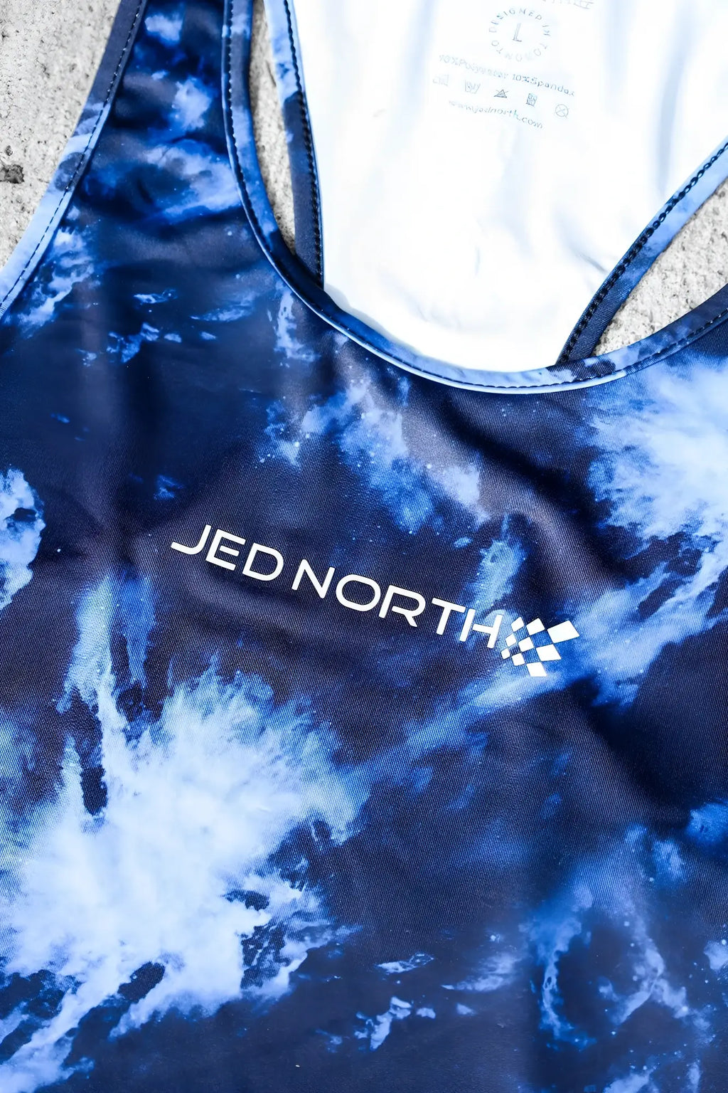 Blue and white tie dye racerback tank top with jed north logo embroidered in white abstract blue muscle stringer