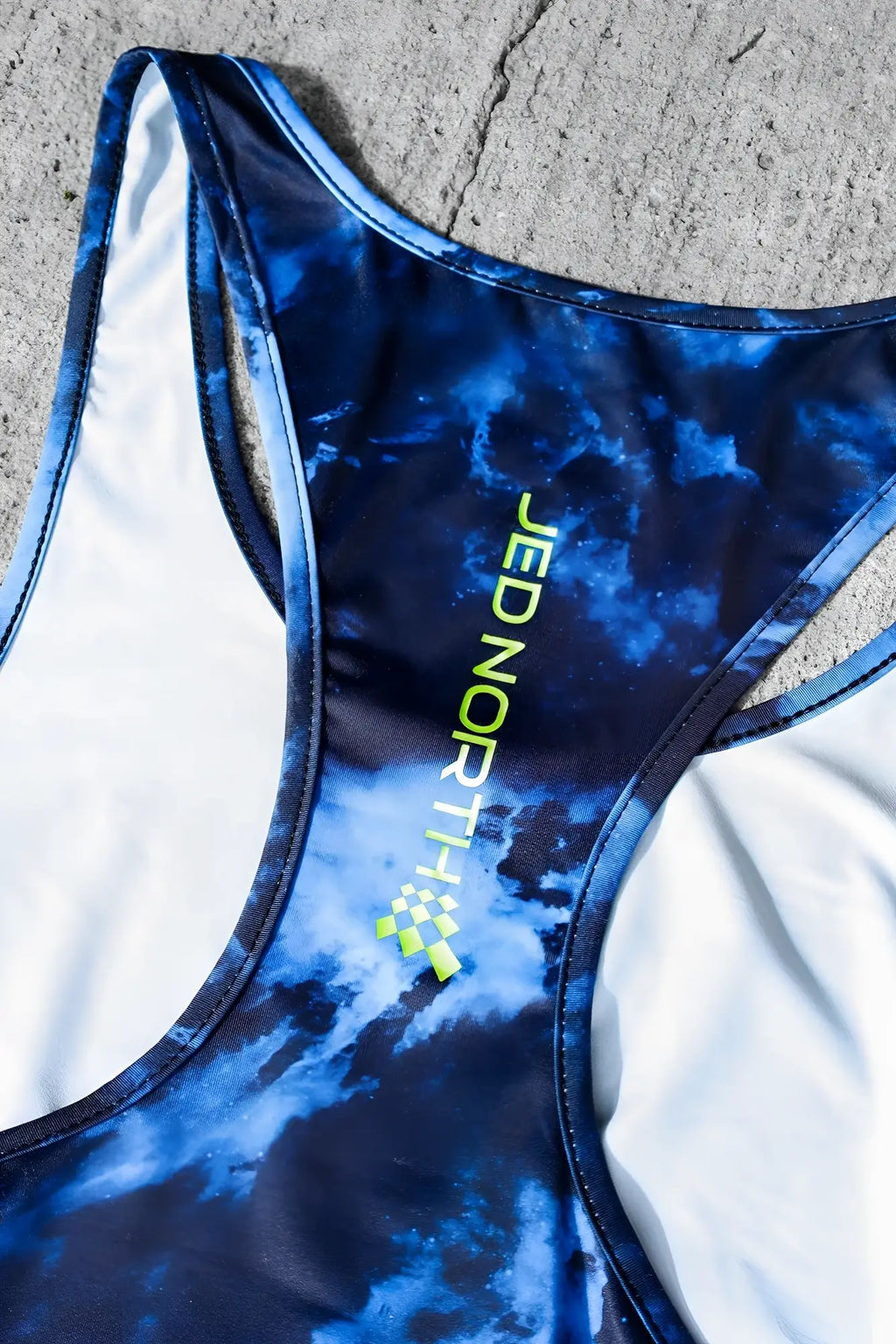 Blue and white tie-dye jed north graphic muscle stringer sports bra with neon green branding for activewear use