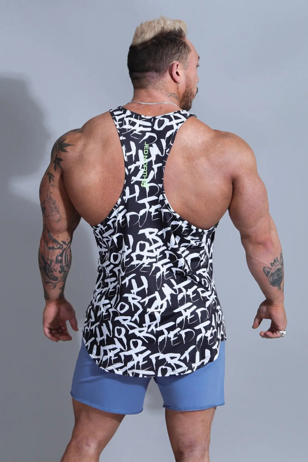 Back side of Jed North graphic muscle stringer tank top in chaotic black with green vertical text and graffiti print