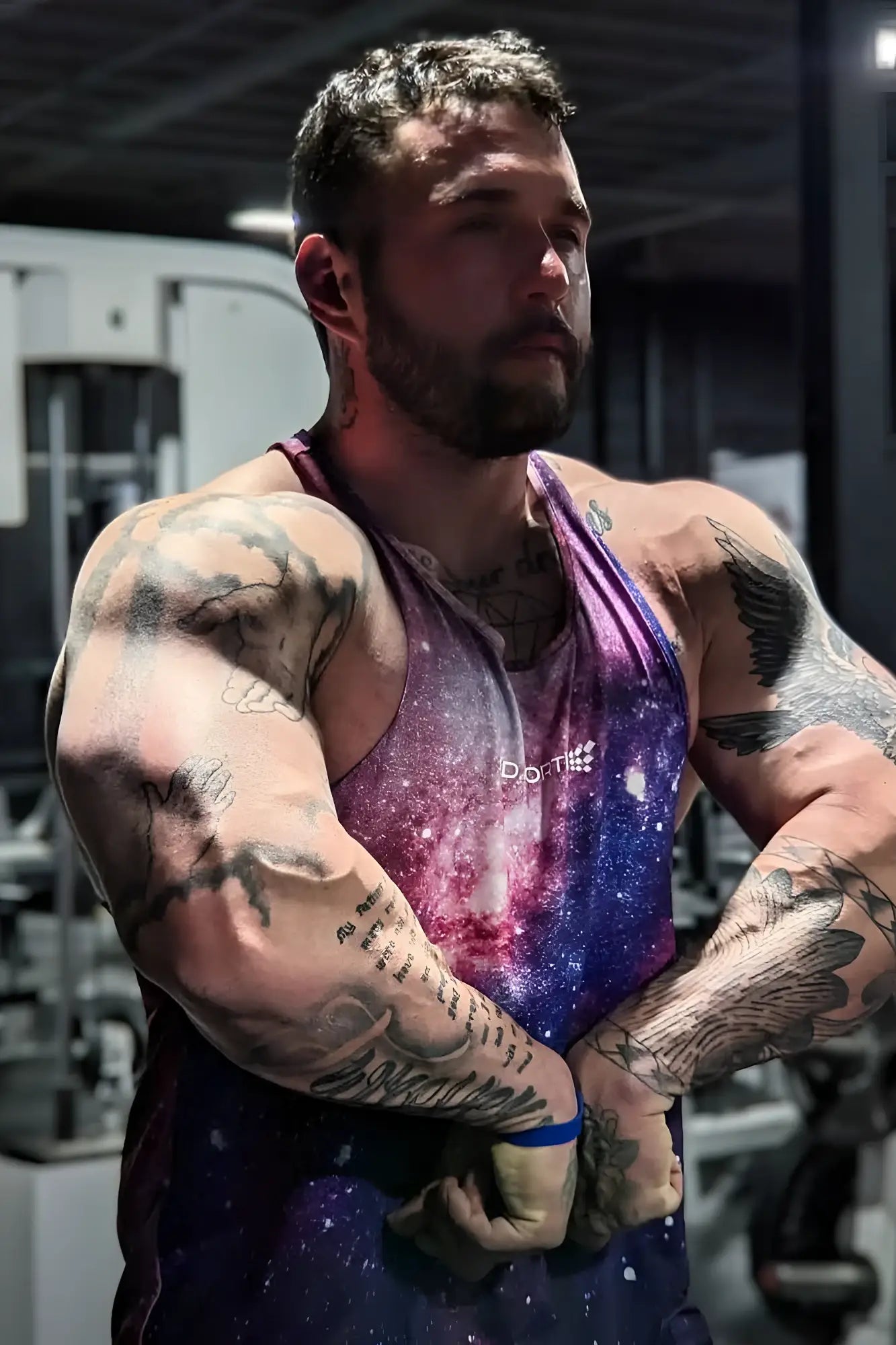 A muscular man wearing a jed north graphic muscle stringer tank top with a galaxy pattern in purple blue and pink hues
