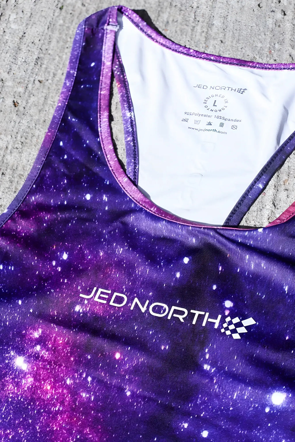 Purple and pink galaxy print racerback tank top with jed north logo in white from the jed north graphic muscle stringer galactic collection