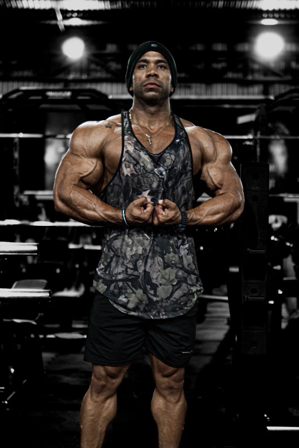Muscular man wearing jed north graphic muscle stringer tank top in hunter camo with black shorts front view