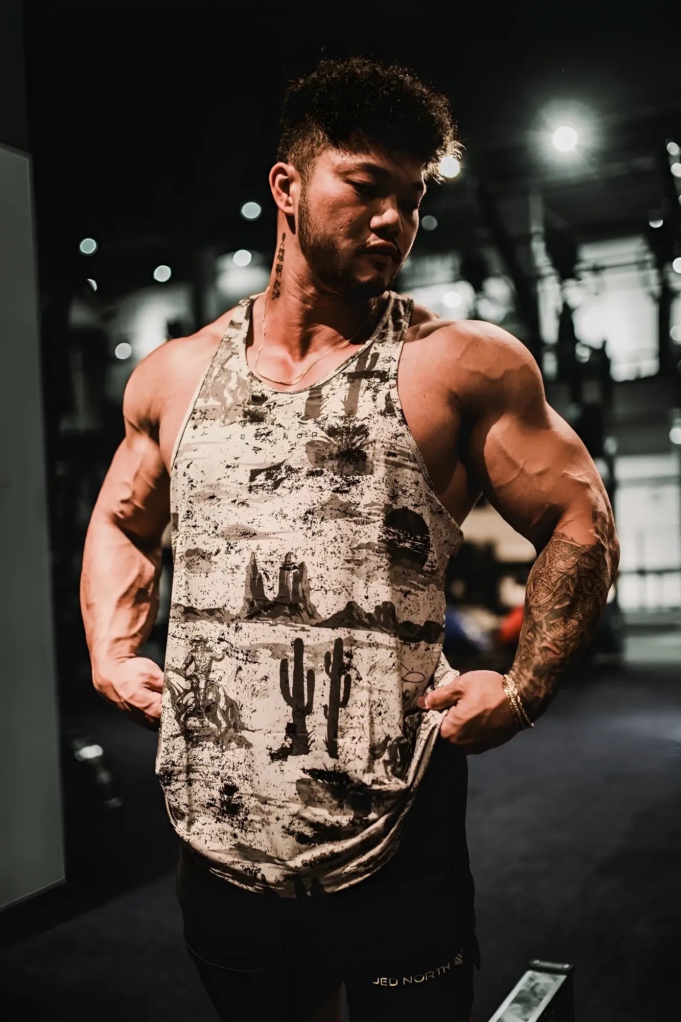 Graphic muscle stringer tank top with rugged outlaw desert print featuring faded cacti and rock formations in beige and black
