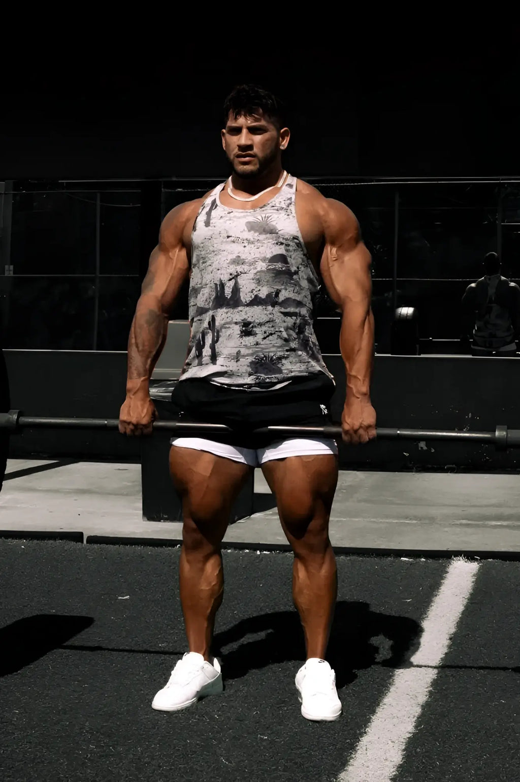 A muscular man wearing a black and white graphic muscle stringer tank top and black shorts with white trim and sneakers