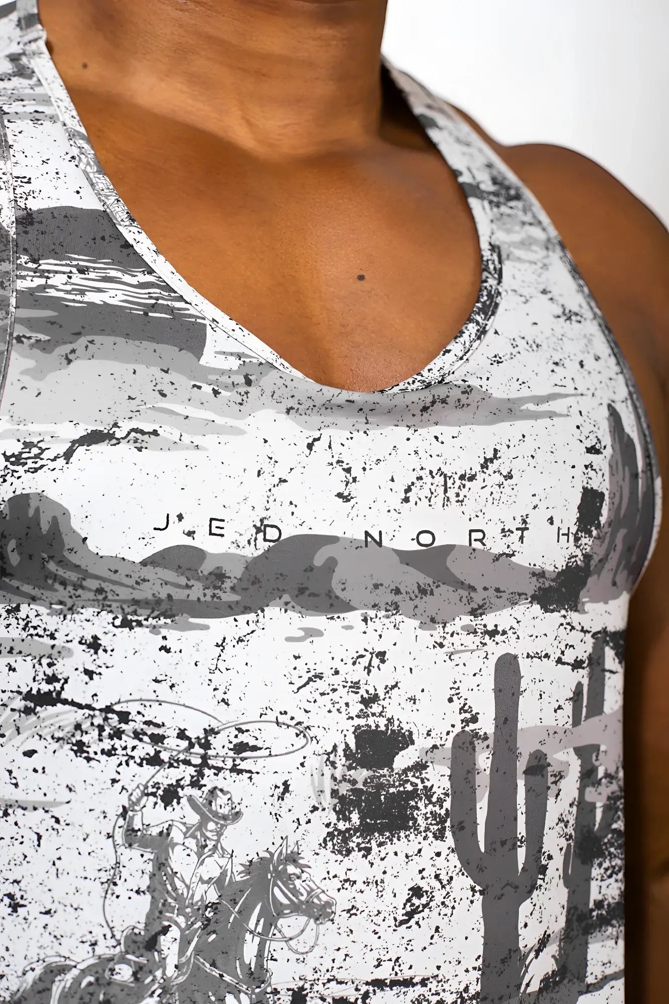 A white and gray distressed graphic muscle stringer tank top with cactus silhouettes and jed north logo on the chest