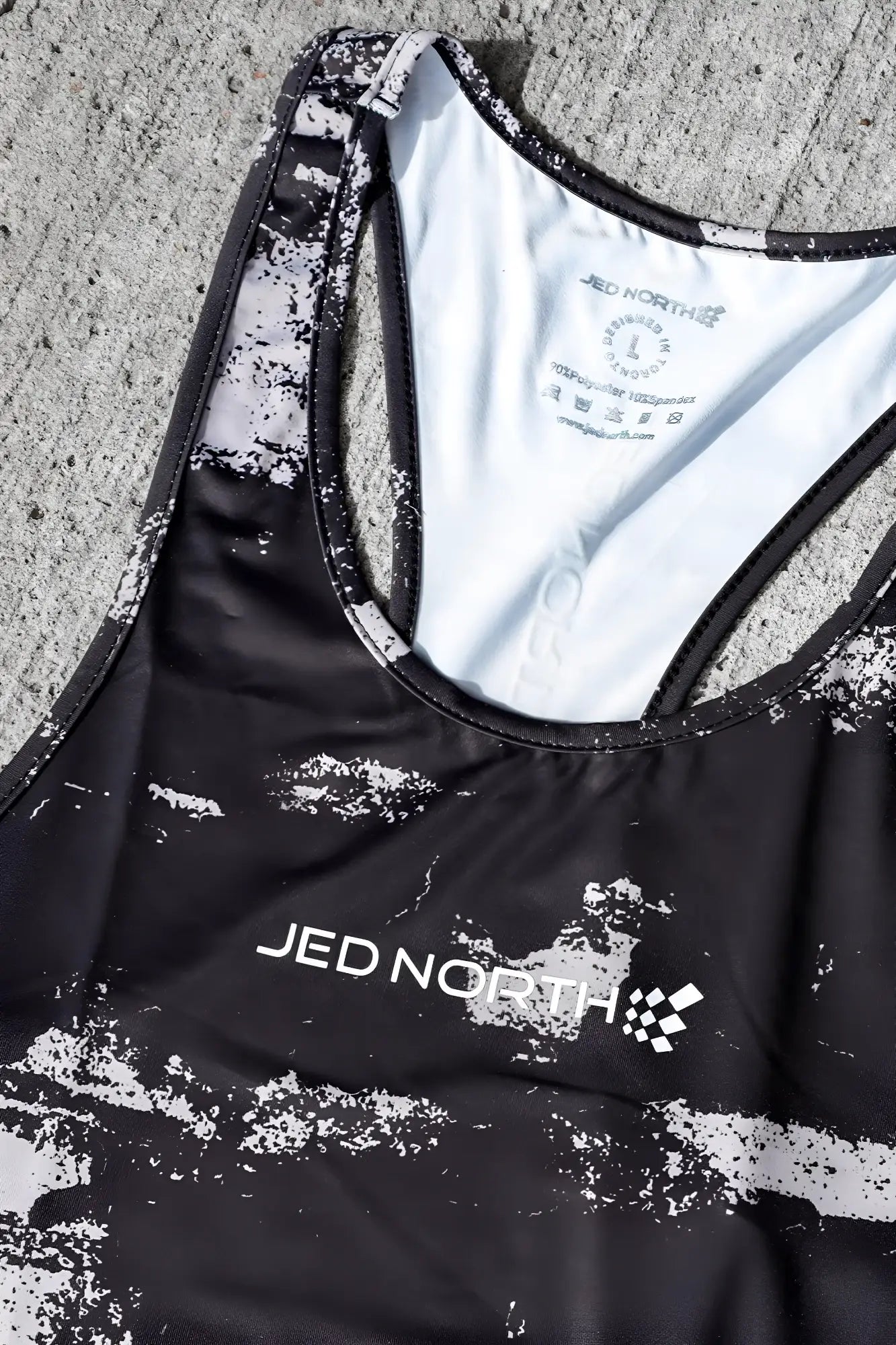 Black and white distressed racerback tank top with jed north branding in silver brush strokes design