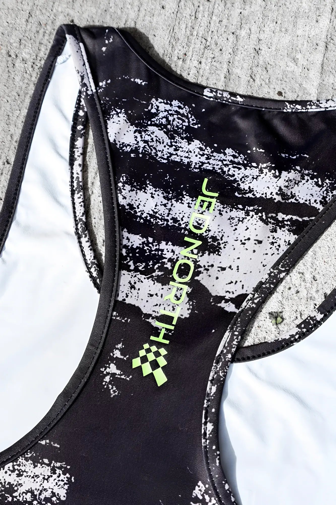 Black and white speckled racerback tank top with neon green jed north branding featuring silver brush strokes design