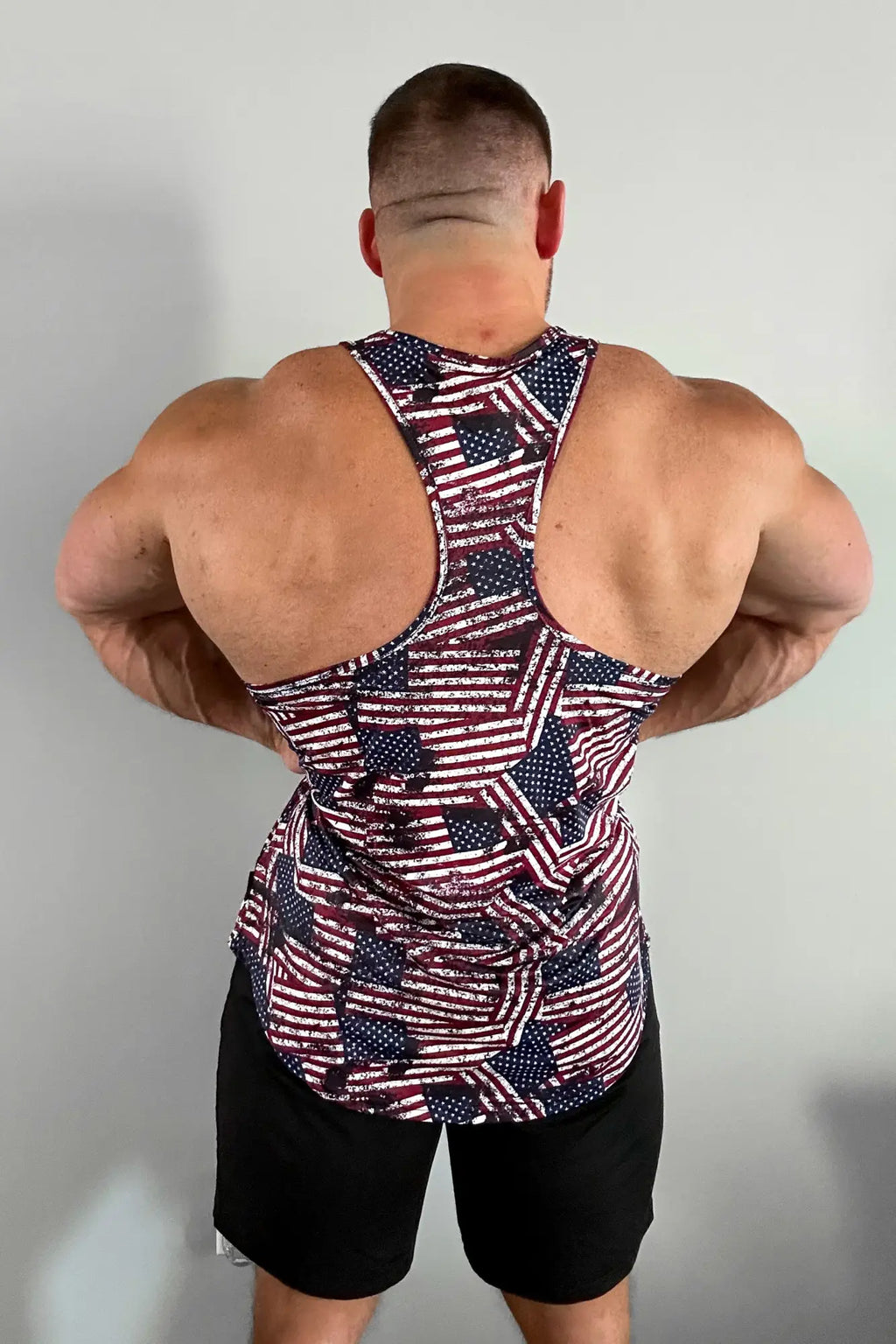 A man wearing a graphic muscle stringer tank top with a distressed usa flag pattern in red white and blue