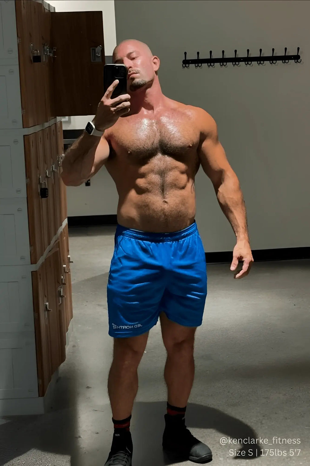 A muscular man wearing jed north jersey mesh 7.5 inch blue gym shorts with a white logo on the left leg