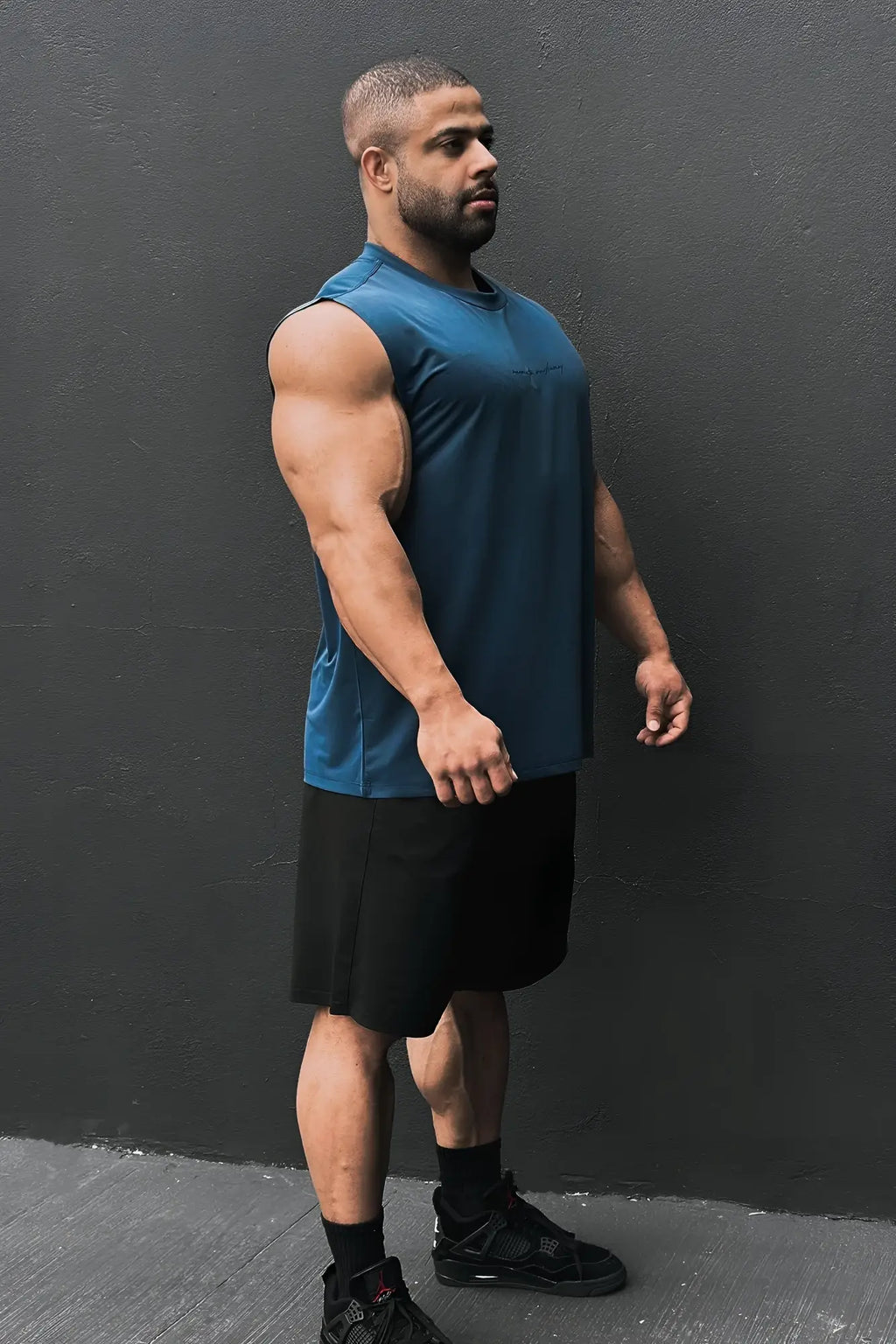A man wearing a navy blue jn active muscle tee with sleeveless design and black shorts for athletic use