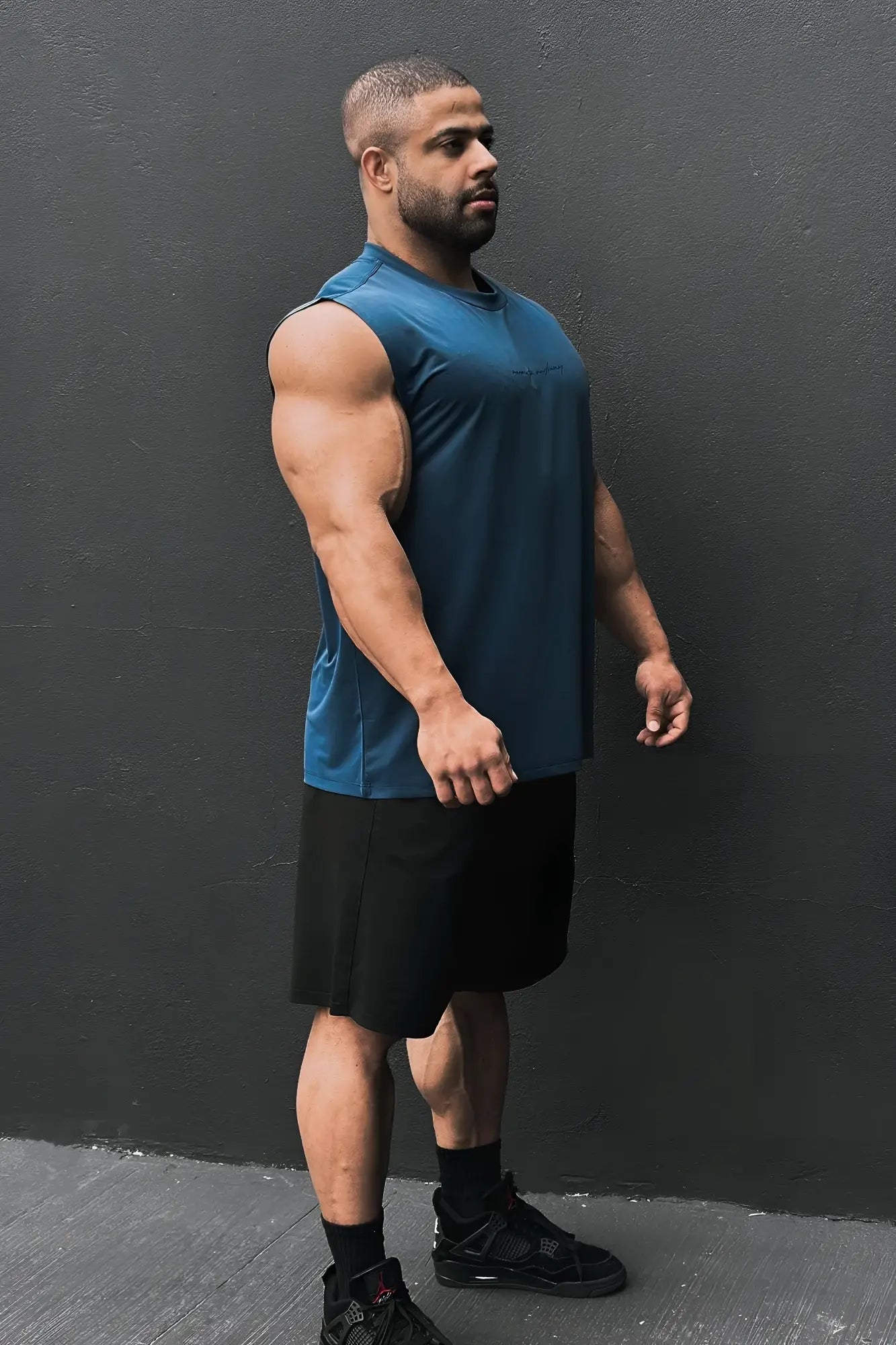 A man wearing a navy blue jn active muscle tee with sleeveless design and black shorts for athletic use