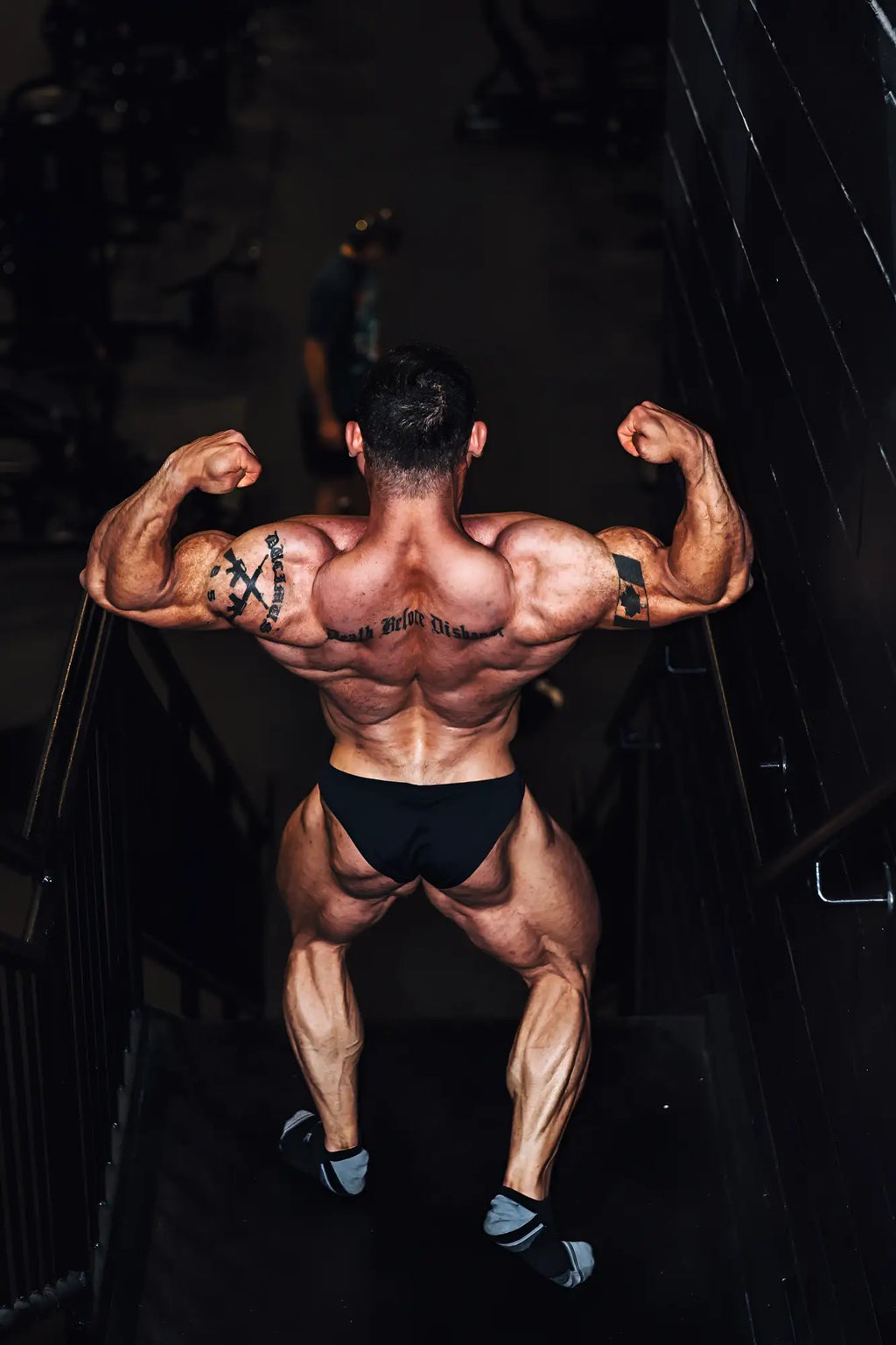 A muscular man with tattoos seen from the back wearing men’s classic physique trunks 2 inch seam black briefs
