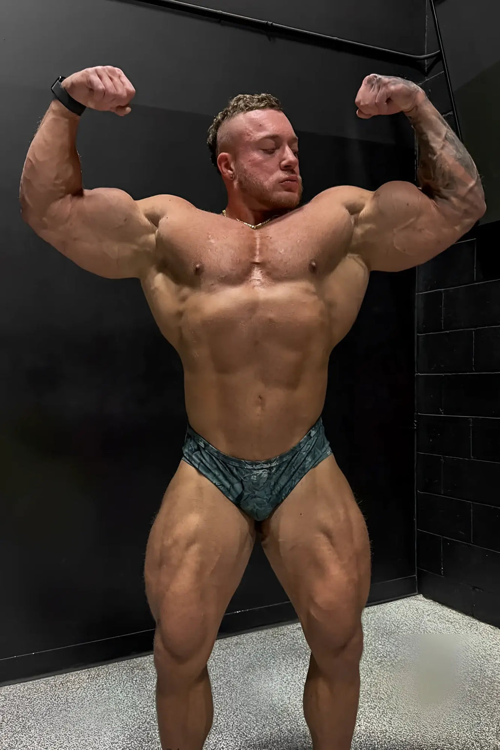 The man is wearing men’s classic physique trunks 2 inch seam in teal camo with a textured fabric design