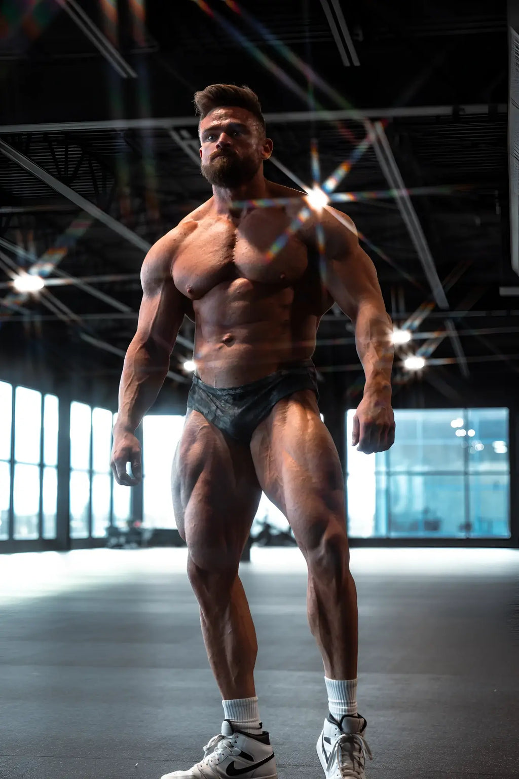 Muscular man wearing men’s classic physique trunks 2 inch seam camo black briefs and white sneakers front view