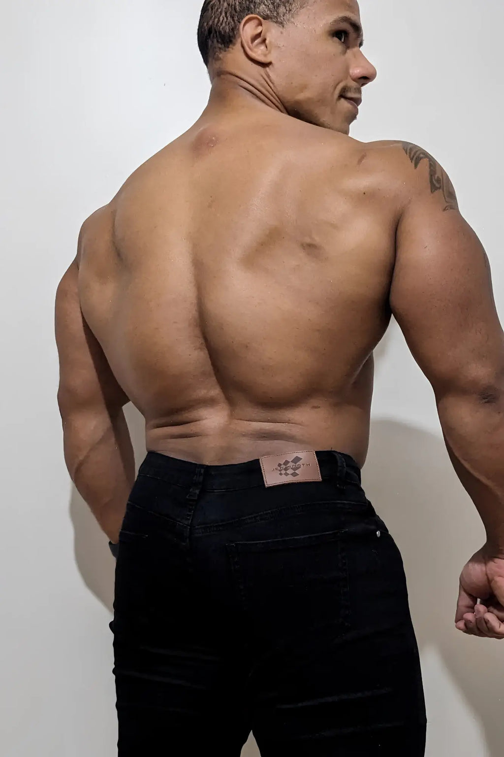 Back view of men’s fitted stretchy black denim jeans with a brown leather patch on the waistband