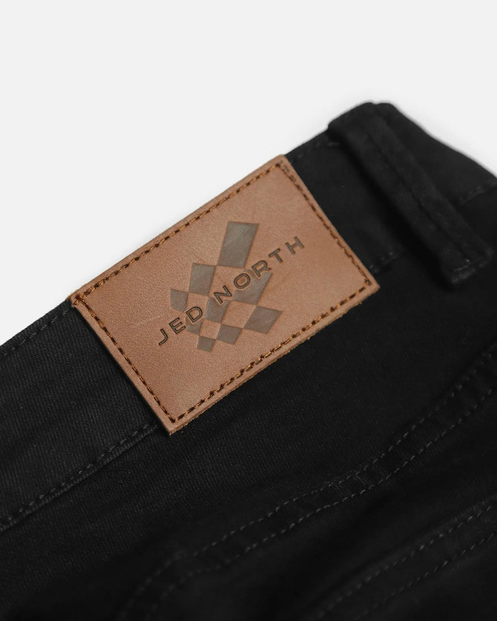 Men’s fitted stretchy black denim jeans showing back side with tan leather patch featuring jed north logo and brand name