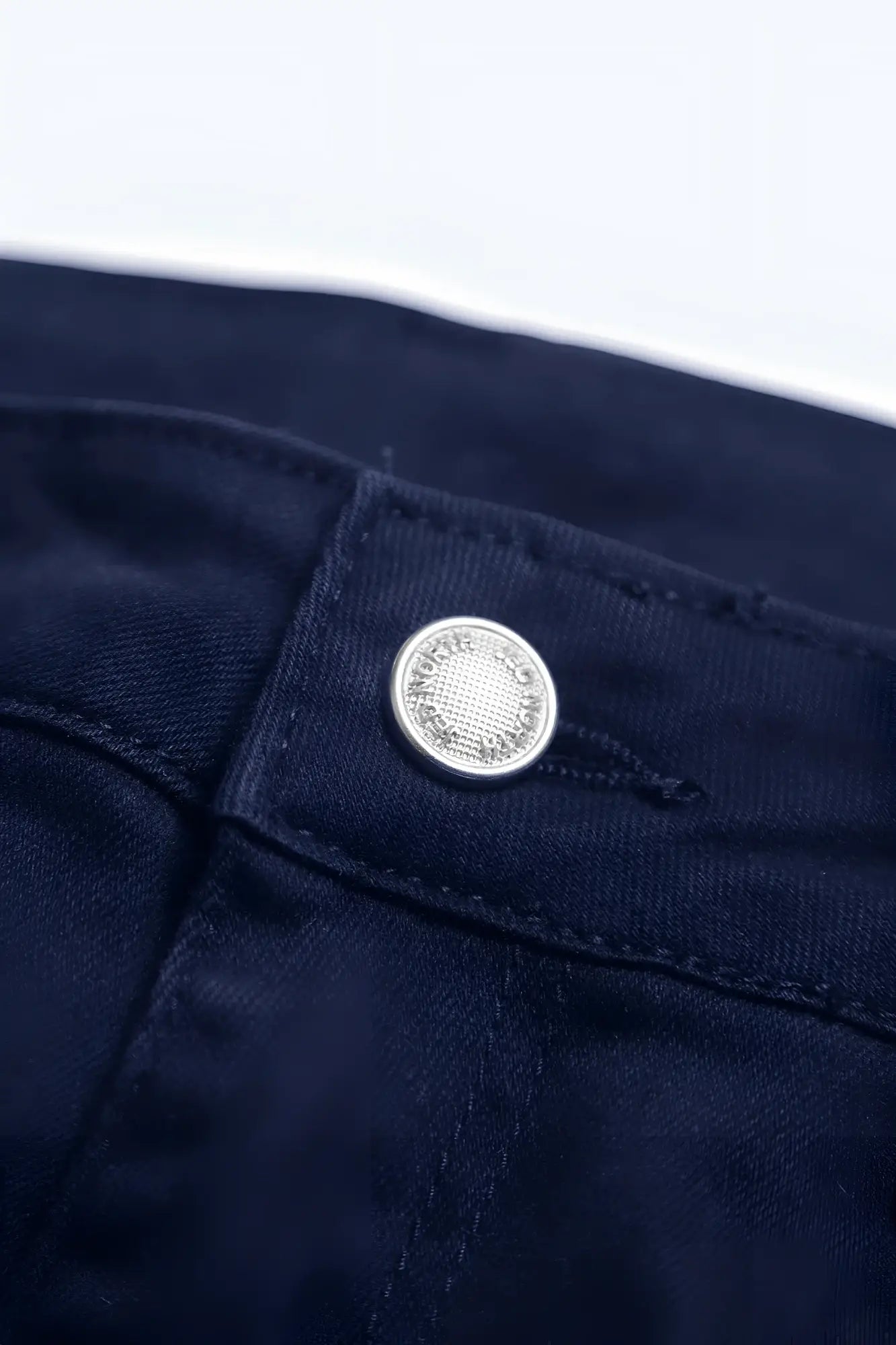 Silver textured button detail on dark blue denim fabric of men’s fitted stretchy navy pants back side