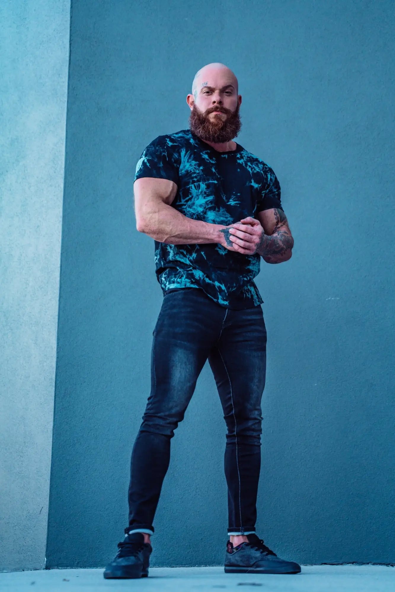 A man wearing men’s premium fitted stretchy faded black jeans paired with a black and teal tie-dye short-sleeved t-shirt