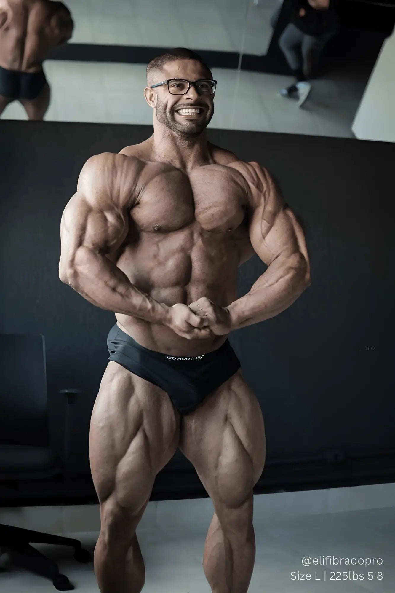 A muscular man with glasses wearing Jed North men’s seamless muscle-fit black briefs and smiling broadly