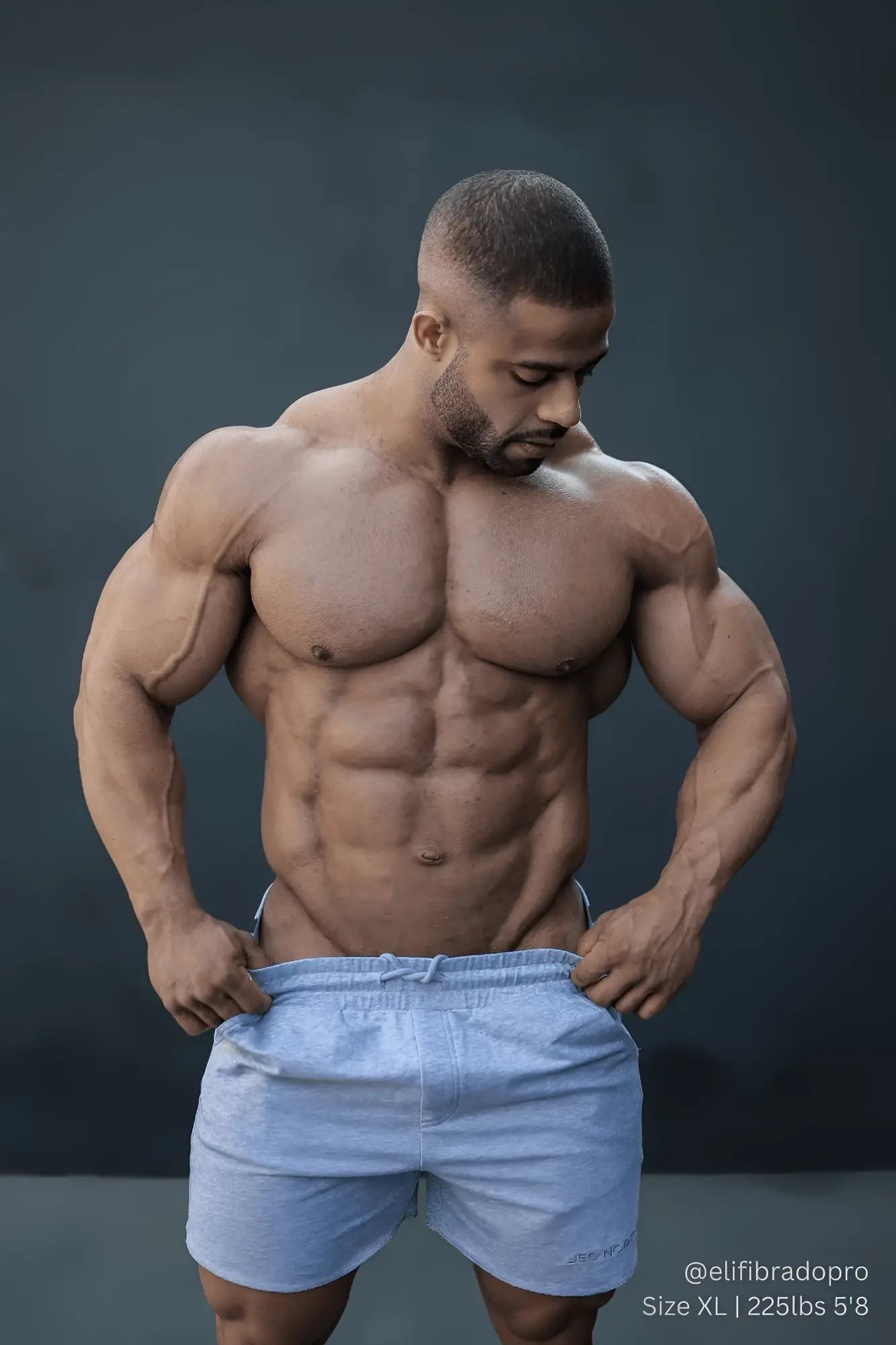 A muscular man wearing light blue athletic shorts showing the back side of Jed North Motion 5 inch varsity sweat shorts gray