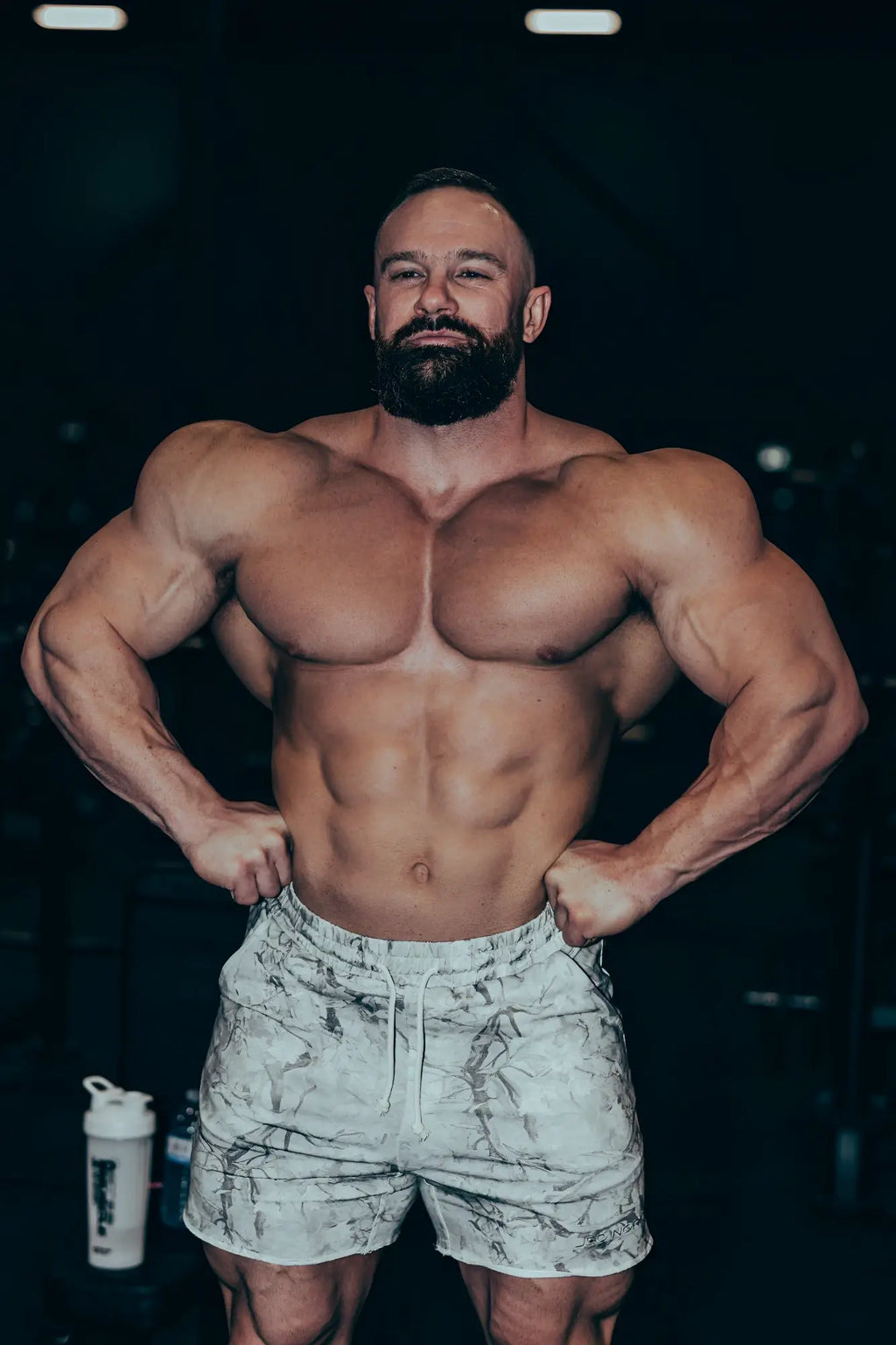 A muscular man wearing white and gray marbled motion 5 inch varsity sweat shorts with leaf camo pattern