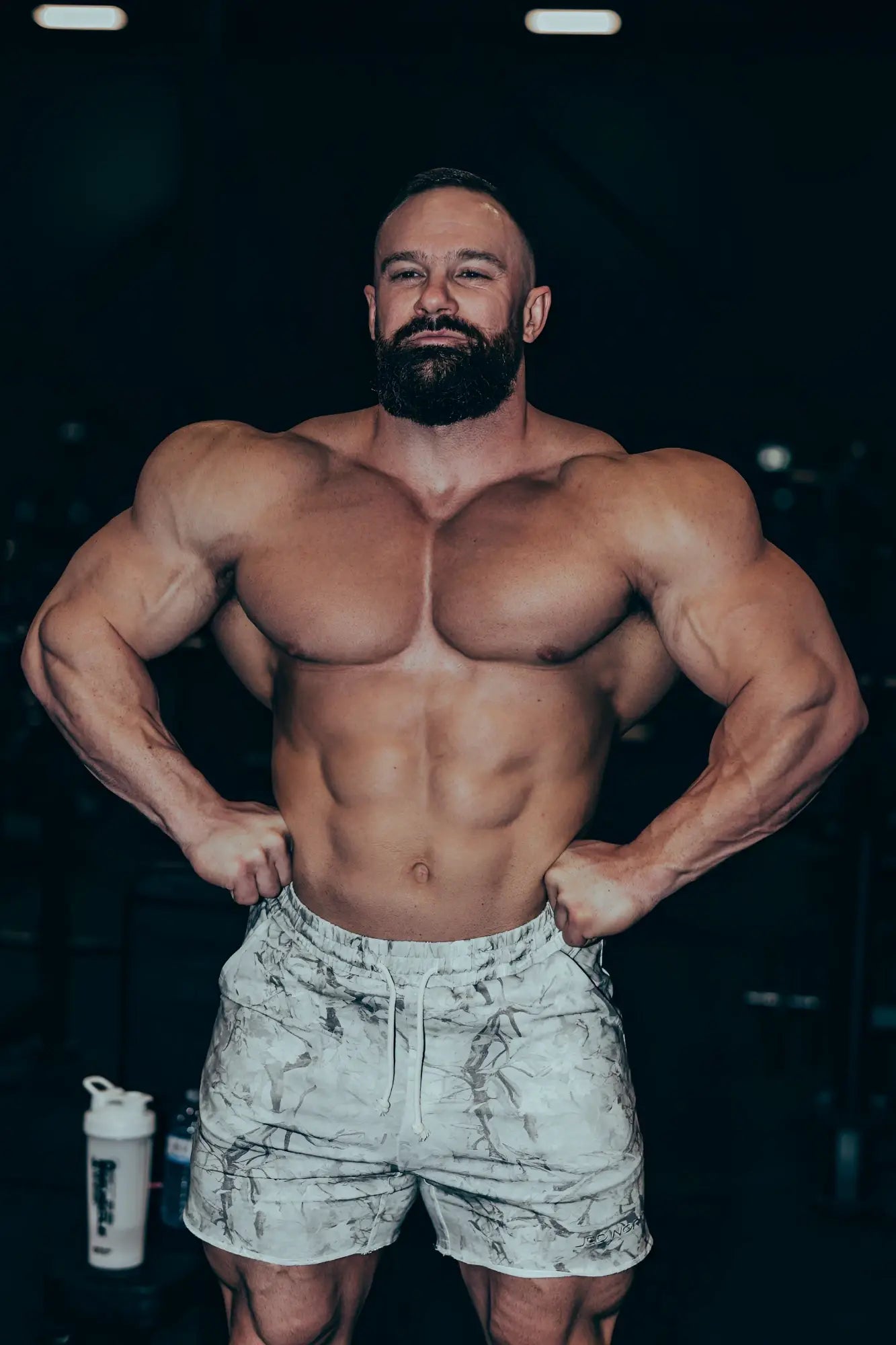 A muscular man wearing white and gray marbled motion 5 inch varsity sweat shorts with leaf camo pattern