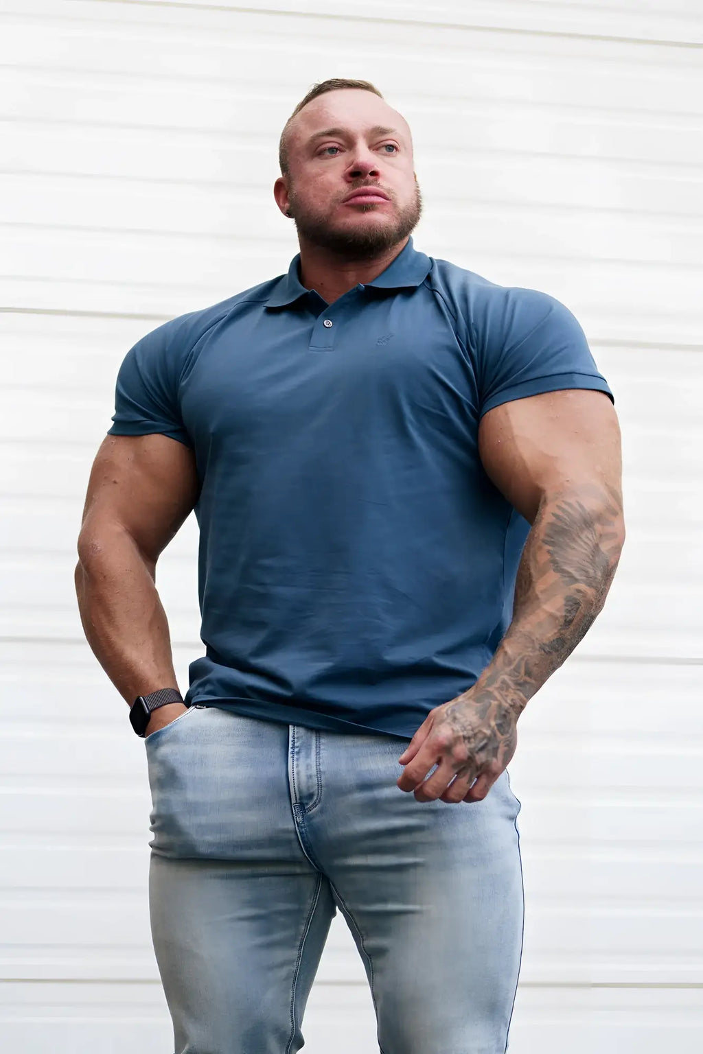 A man wearing a muscle fit all-day polo t-shirt in storm blue with short sleeves and a button placket collar
