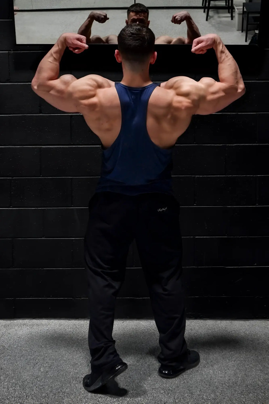 Muscular man wearing jed north performance max bodybuilding stringer in denim blue with black athletic pants