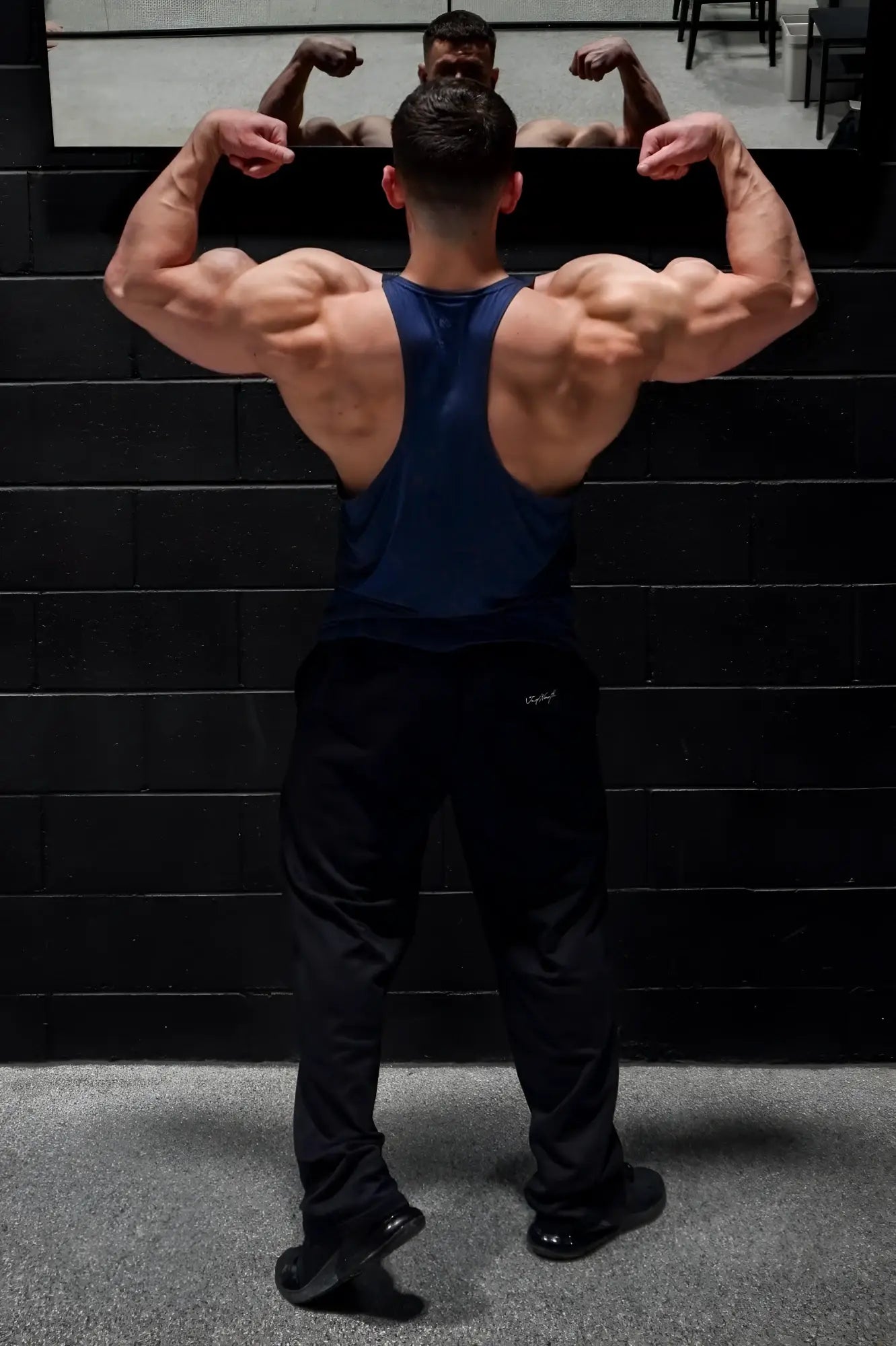 Muscular man wearing jed north performance max bodybuilding stringer in denim blue with black athletic pants