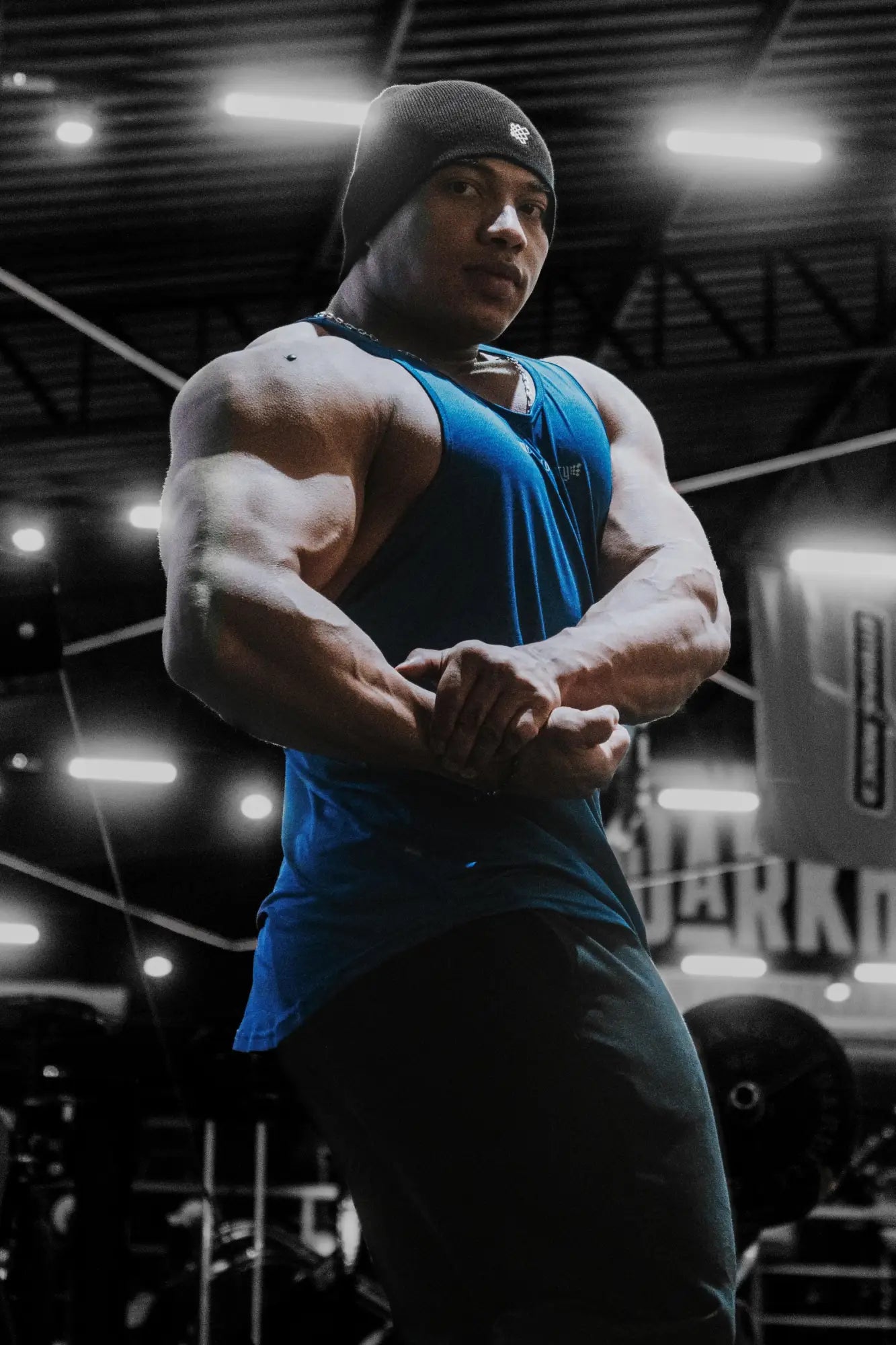 A muscular man wearing a jed north performance max bodybuilding stringer in denim blue with a black beanie
