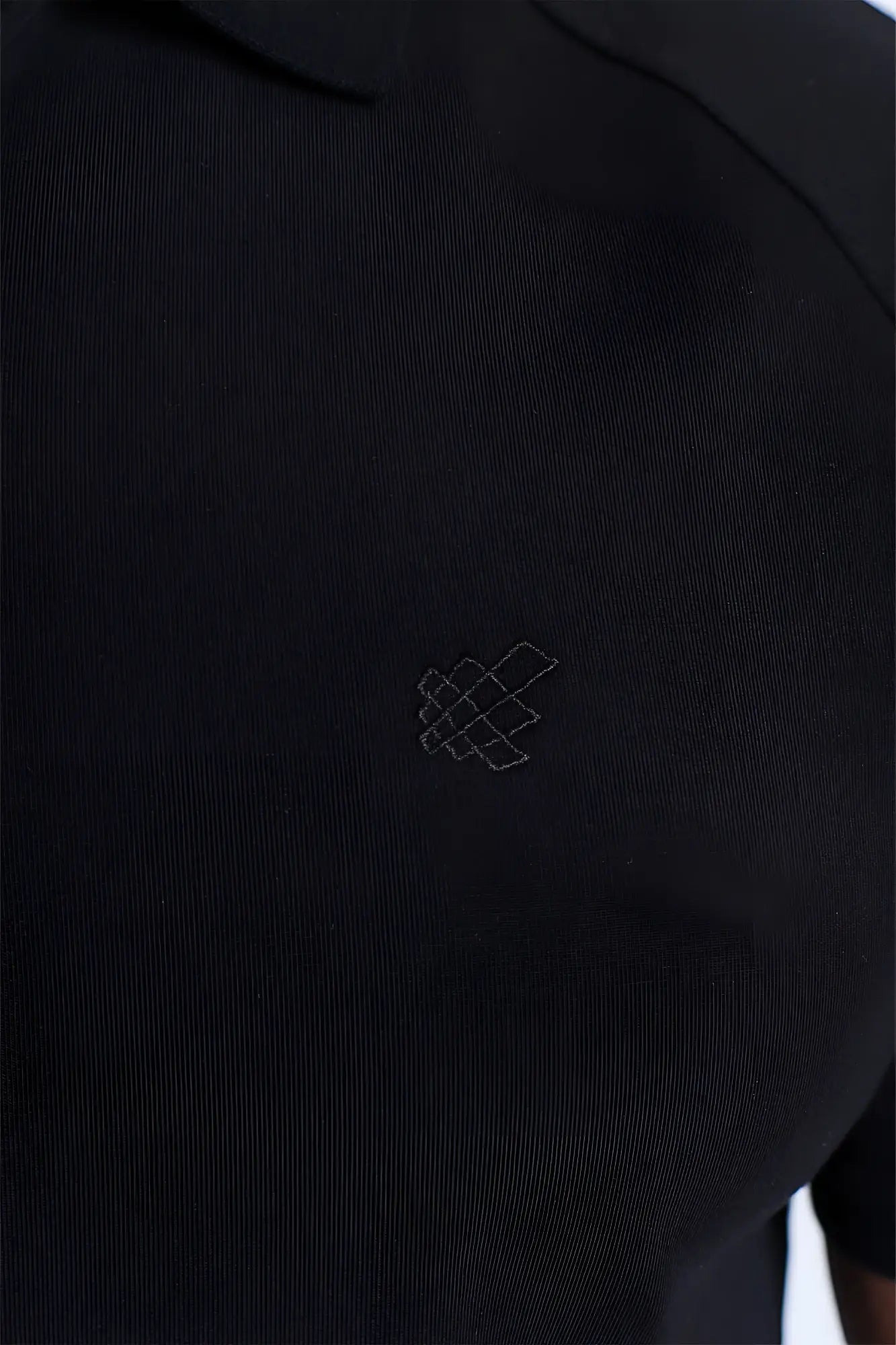 Premium muscle-fit black polo tee with textured fabric and subtle white geometric logo embroidered on the chest