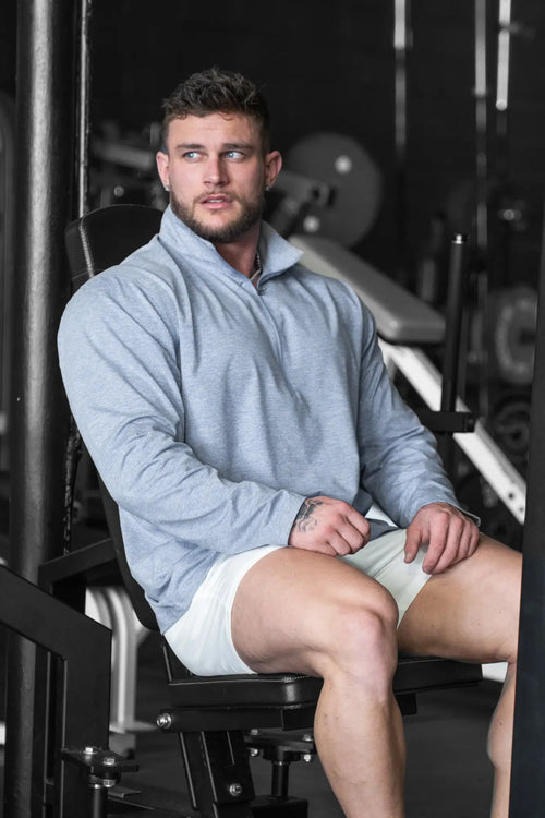A man wearing a heather blue quarter-zip training long sleeve pullover with a half-zip collar and white shorts