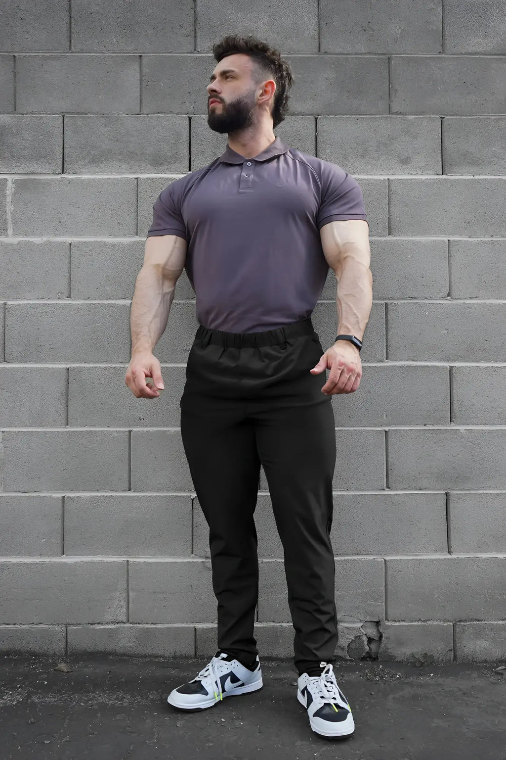 A man wearing a fitted purple polo shirt with black jed north quick-dry tech pants designed for athletic use