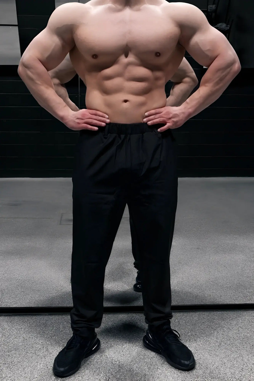 A muscular man wearing jed north quick-dry tech pants in black and matching black sneakers showcasing athletic wear
