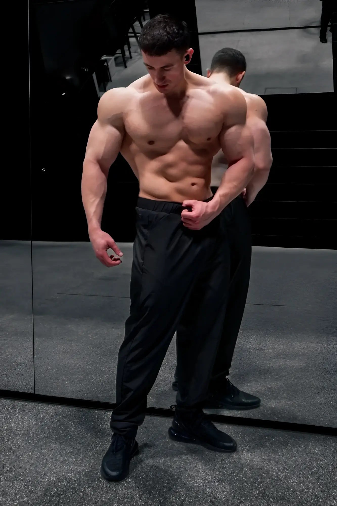A muscular man wearing jed north quick-dry tech pants in black and matching black sneakers displaying athletic wear