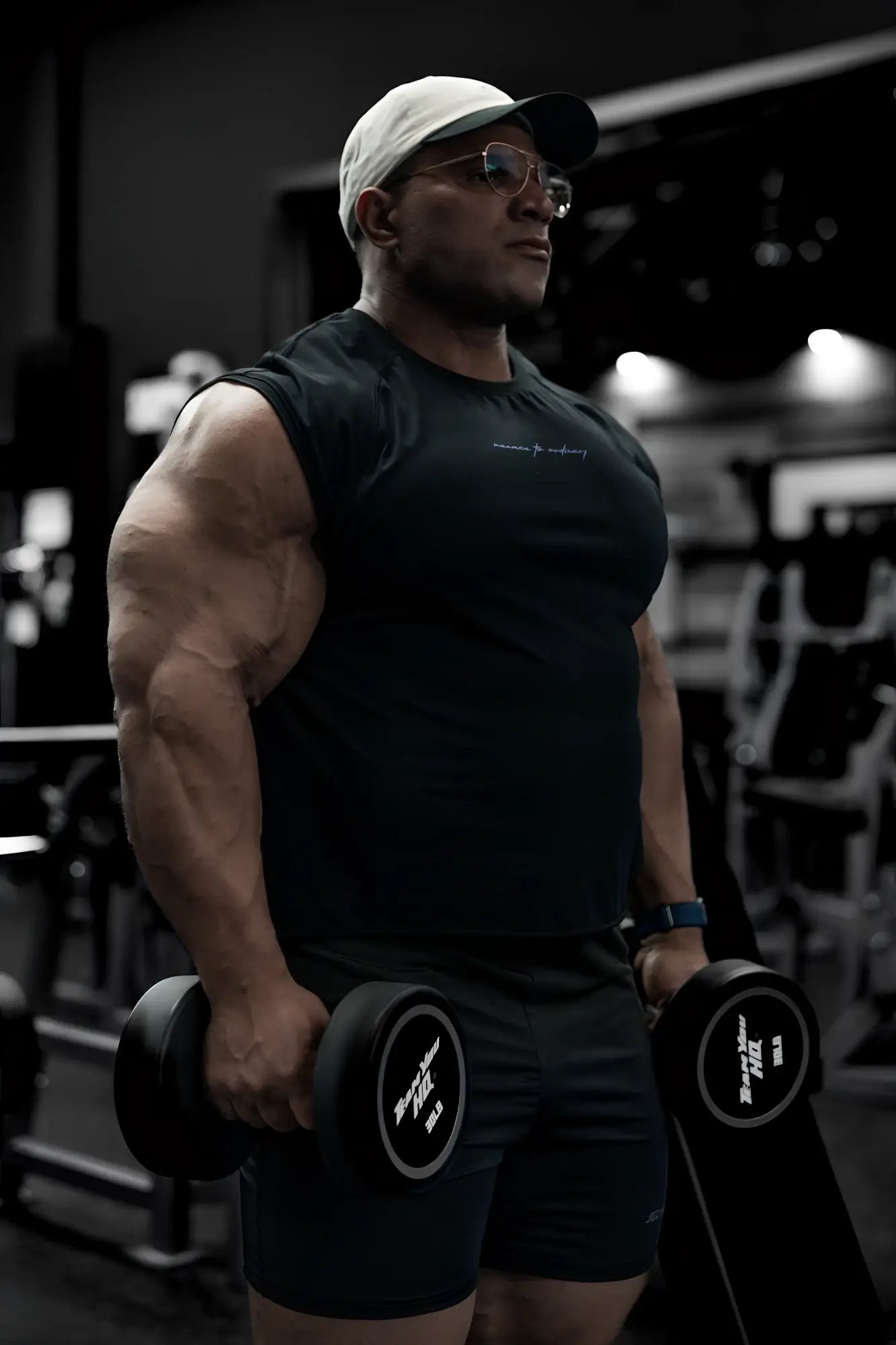 Black dumbbells with white circular labels featuring black text next to an all black raglan sleeveless muscle tank
