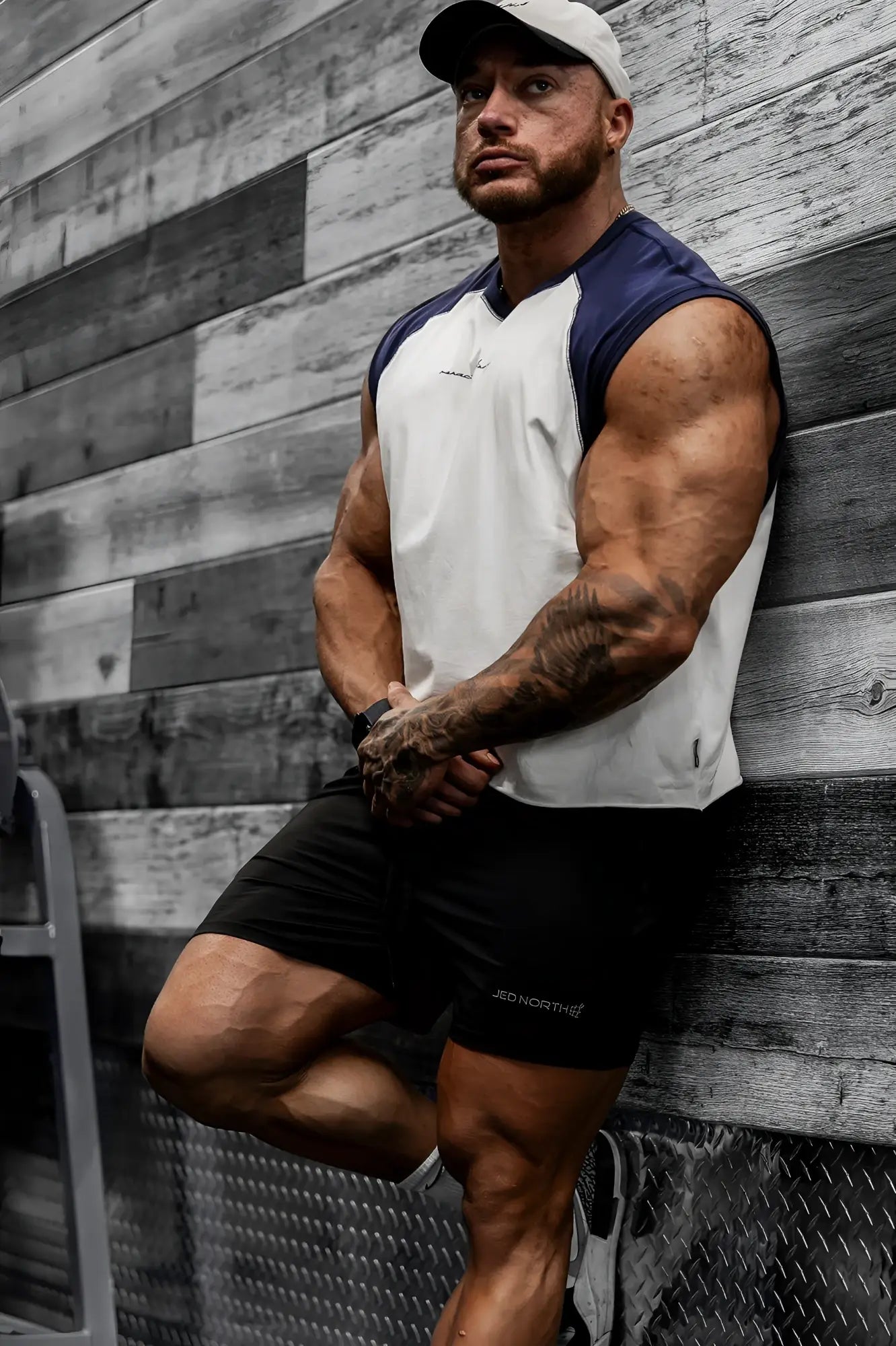 A man wearing a navy raglan sleeveless muscle tank with white and black shorts featuring the jeo north logo